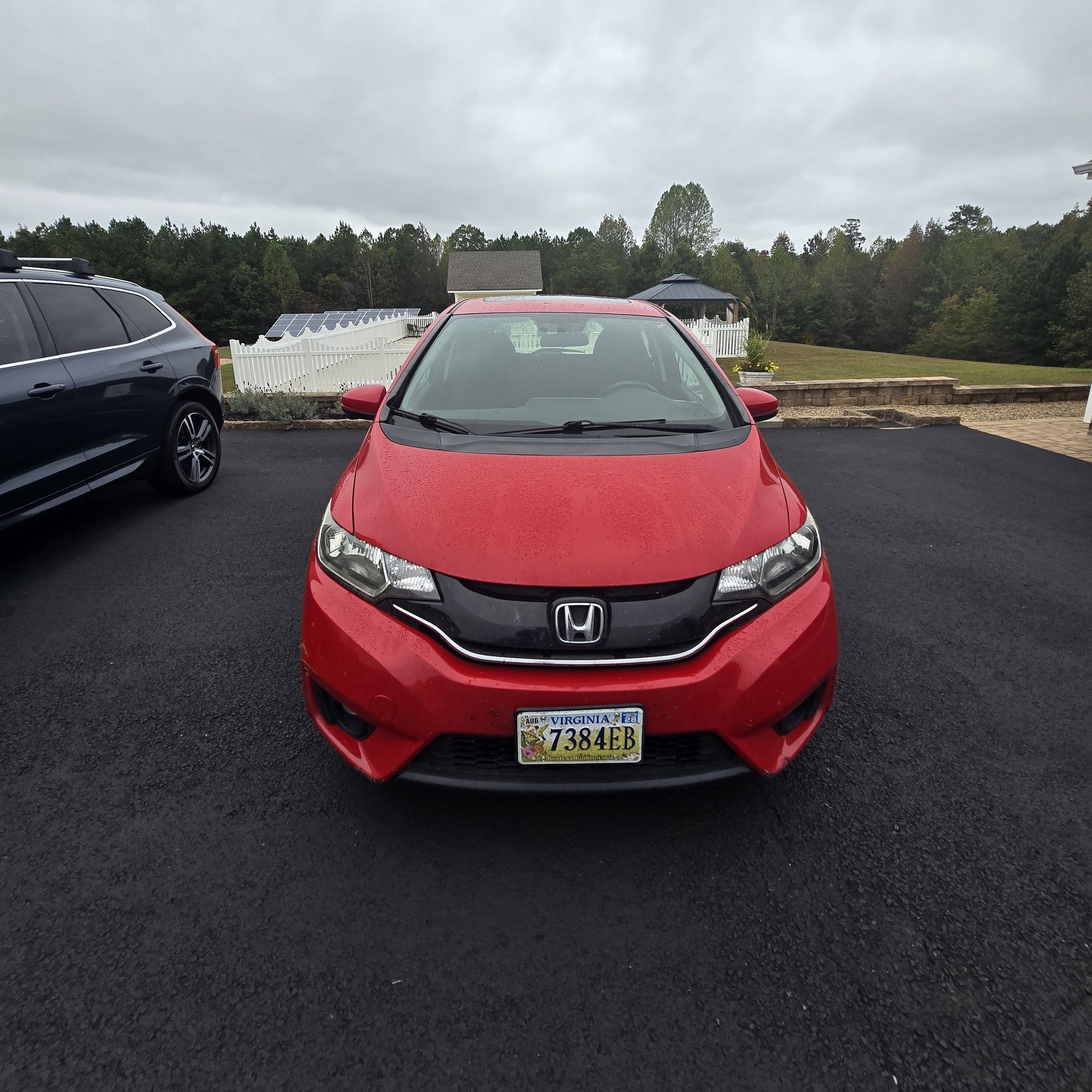 Red Honda Fit parked on a blacktop driveway on an overcast day.