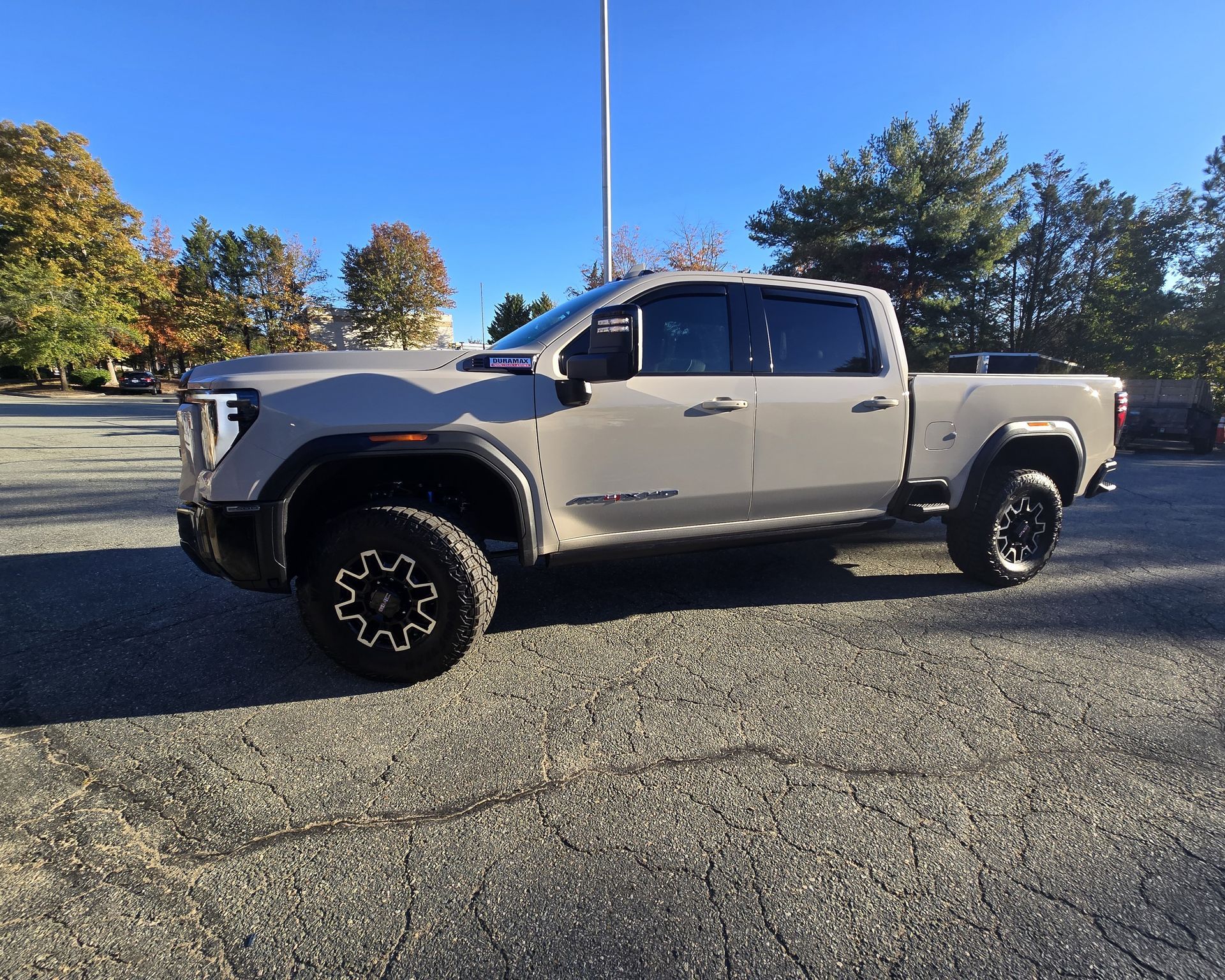 Gray GMC truck parked on asphalt, large tires, overcast sky, trees in the background.