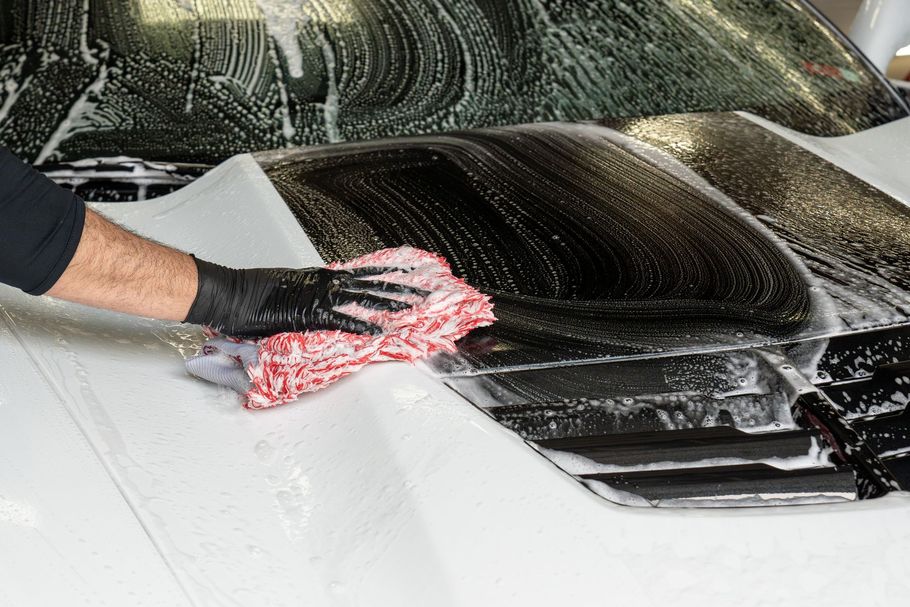 A person is cleaning the hood of a car with a cloth .