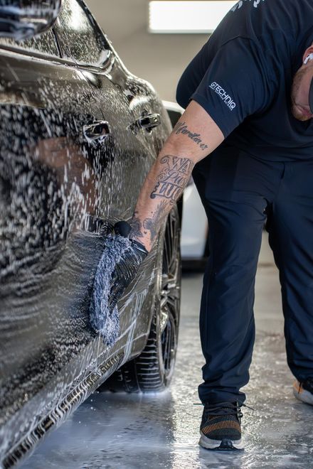 A man is washing a car with a sponge in a garage .