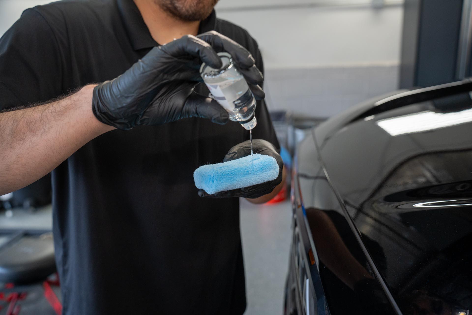 A man is applying a coating to a black car .