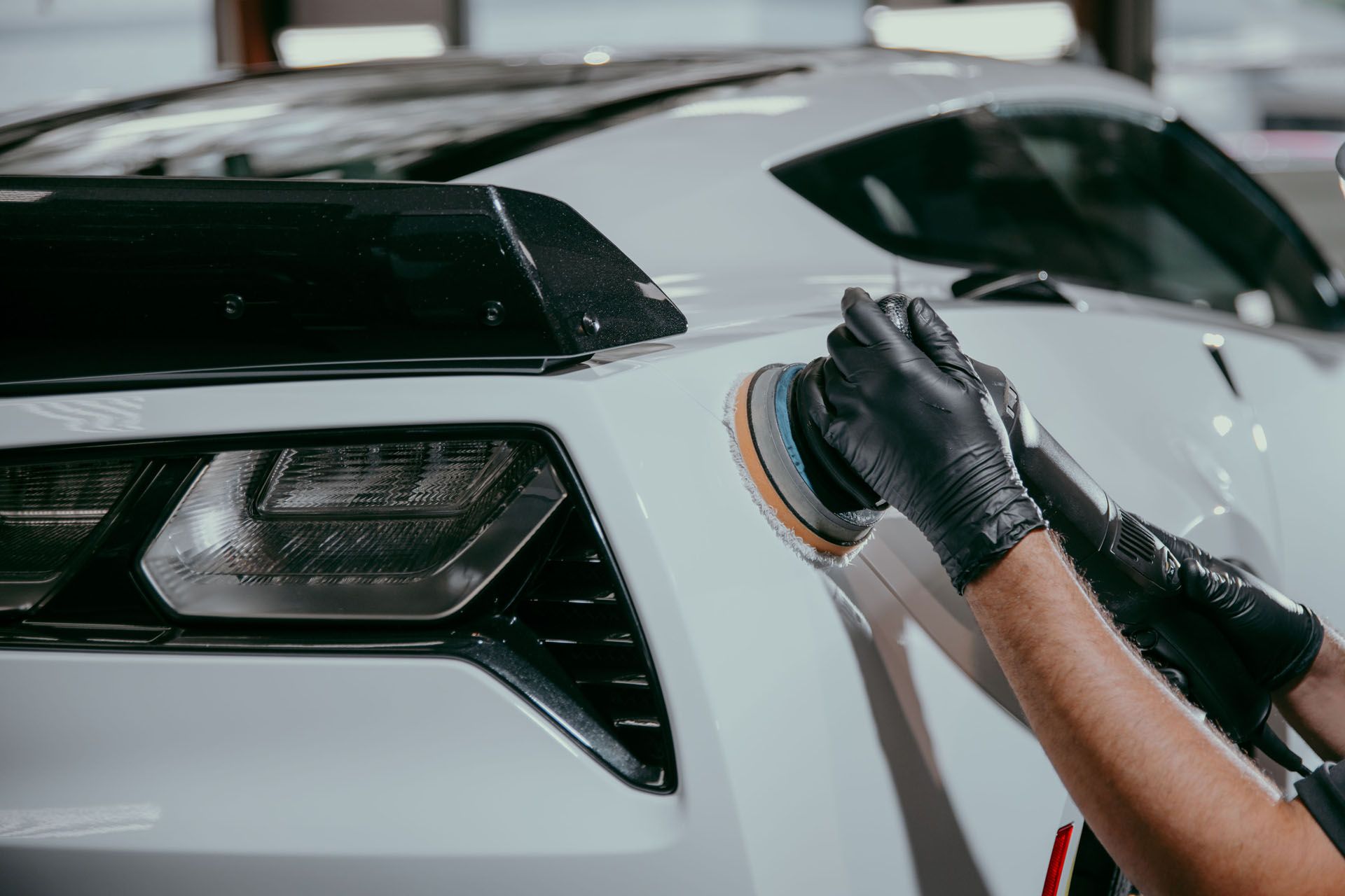 A person is polishing a white car with a sander .