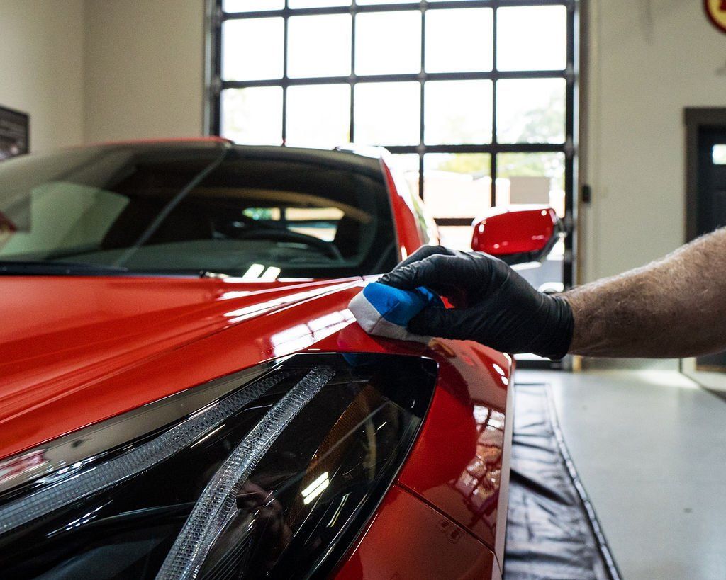 Gloved hand applying polish to a red sports car in a garage