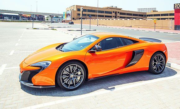 Orange sports car parked on a rooftop deck under bright sunlight