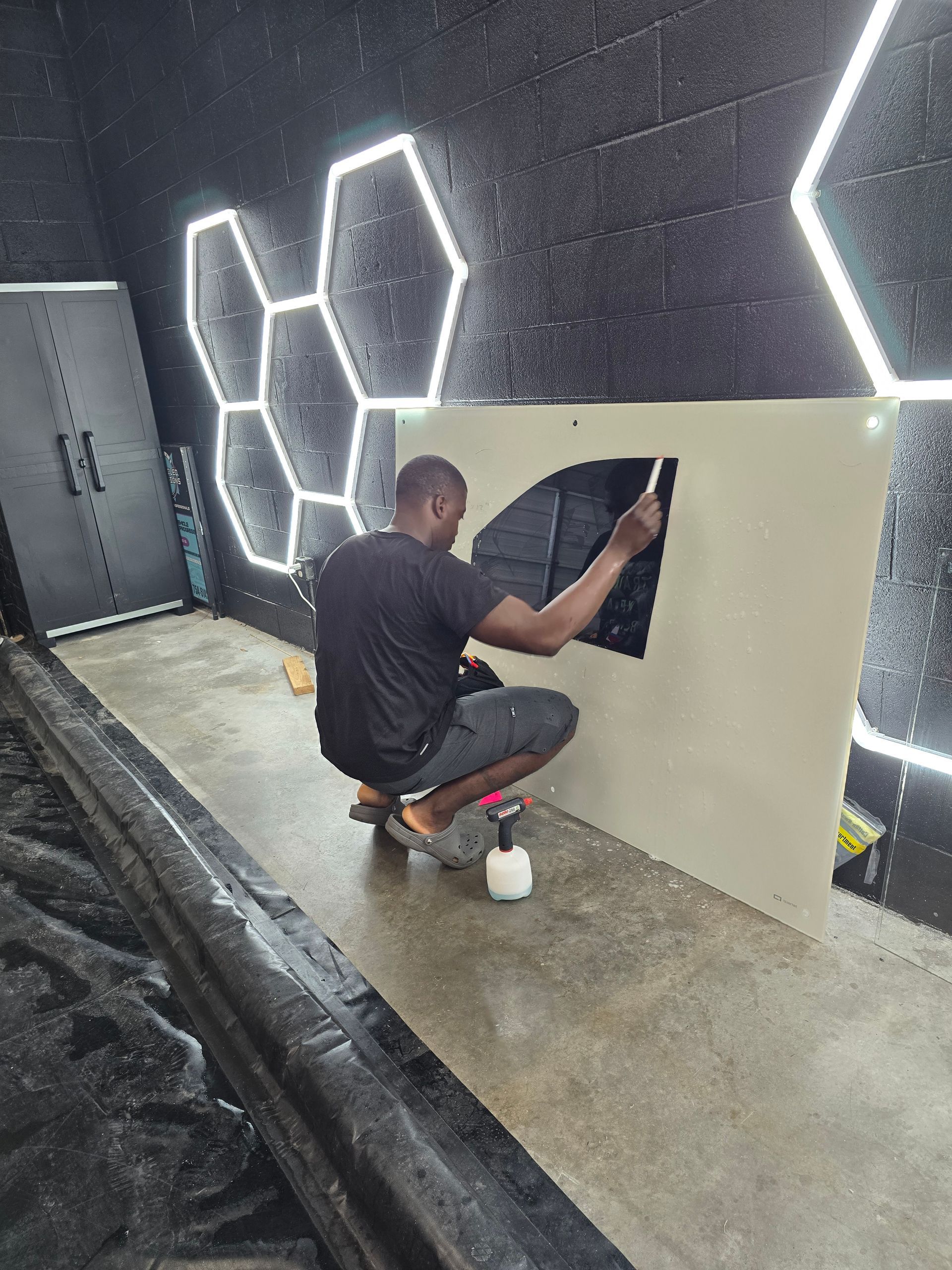 Man applying black material to a white surface, working in a room with hexagonal LED lights on a black wall.