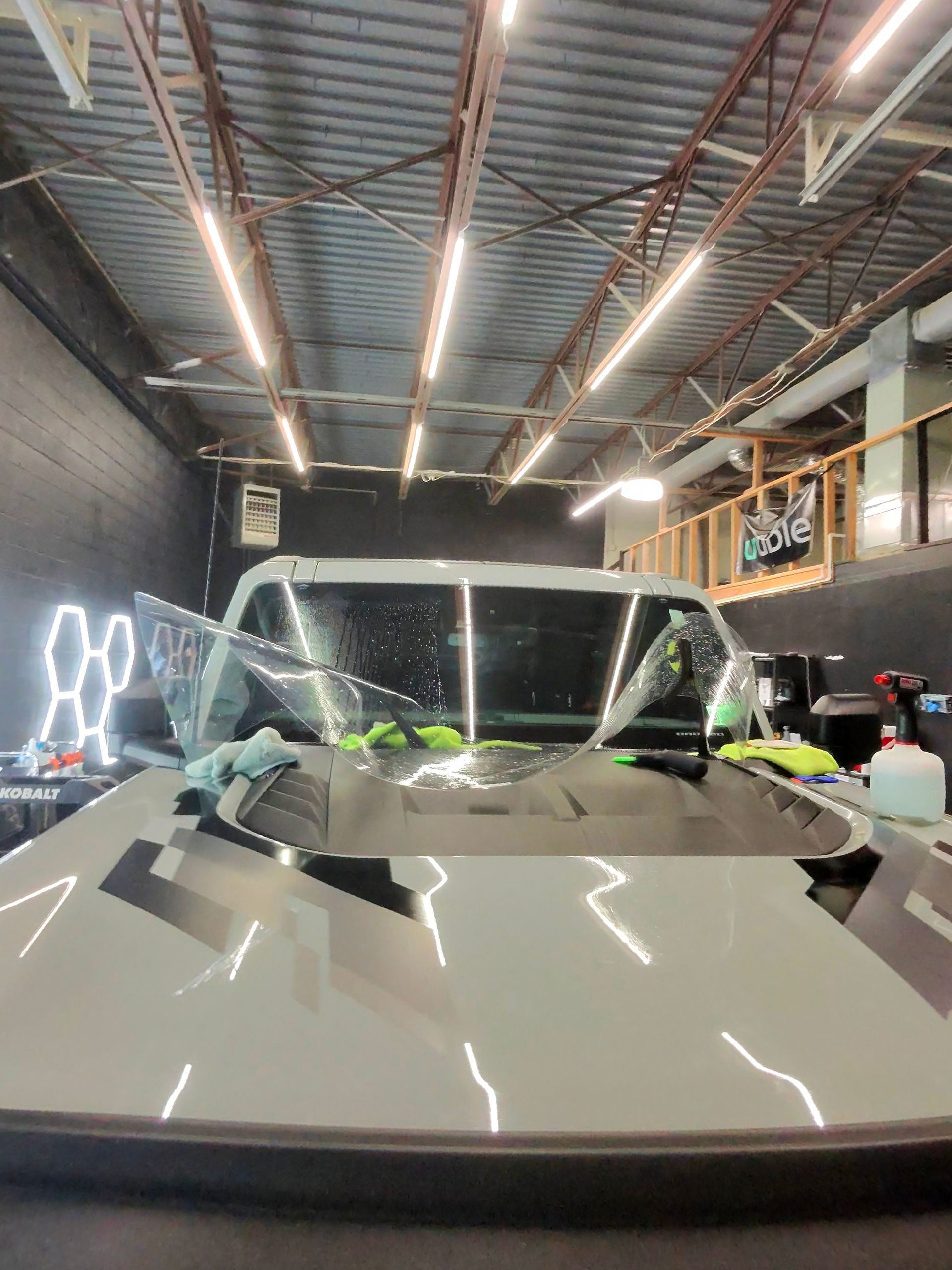 A white SUV with window film being applied in a garage with bright overhead lights.