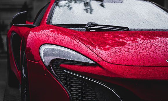 Close-up of a red sports car front with rain droplets and black accents