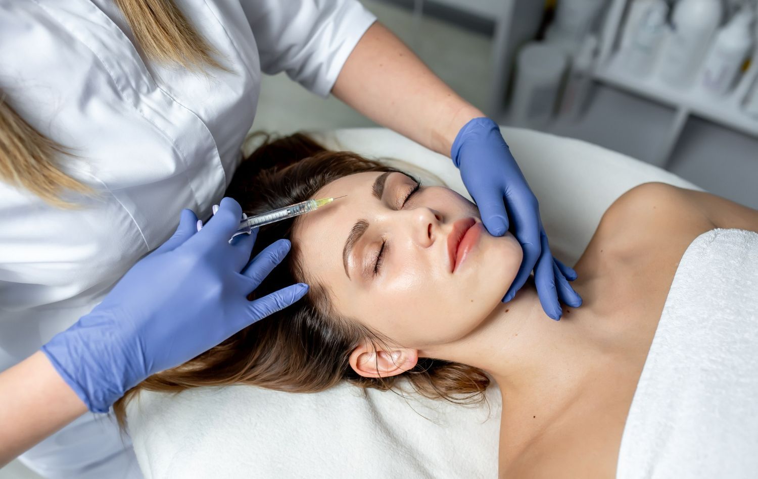 Person receiving facial injection; clinician with gloves administering the procedure. White setting.