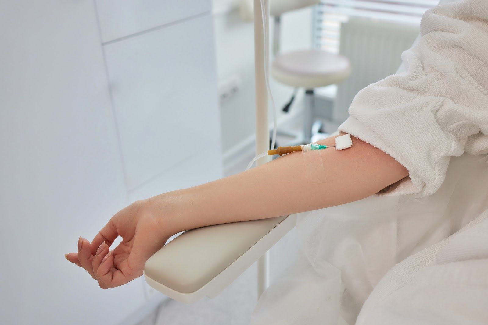 Person with IV drip in their arm, sitting in a medical setting, wearing a white robe.