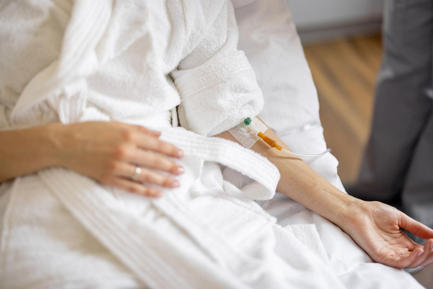 Person in white robe with IV in arm, resting on a bed.