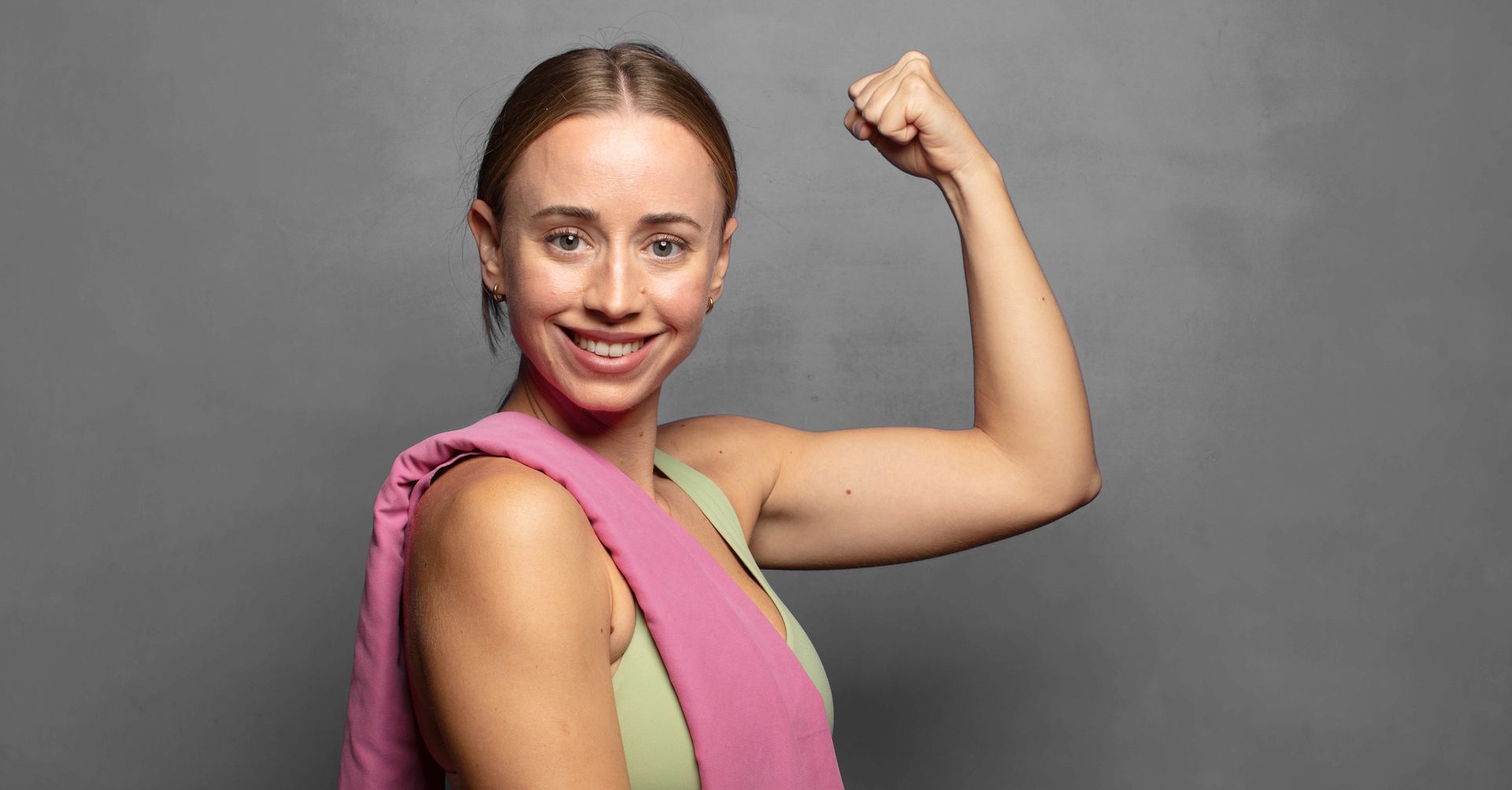 A woman is flexing her muscles in front of a gray background.
