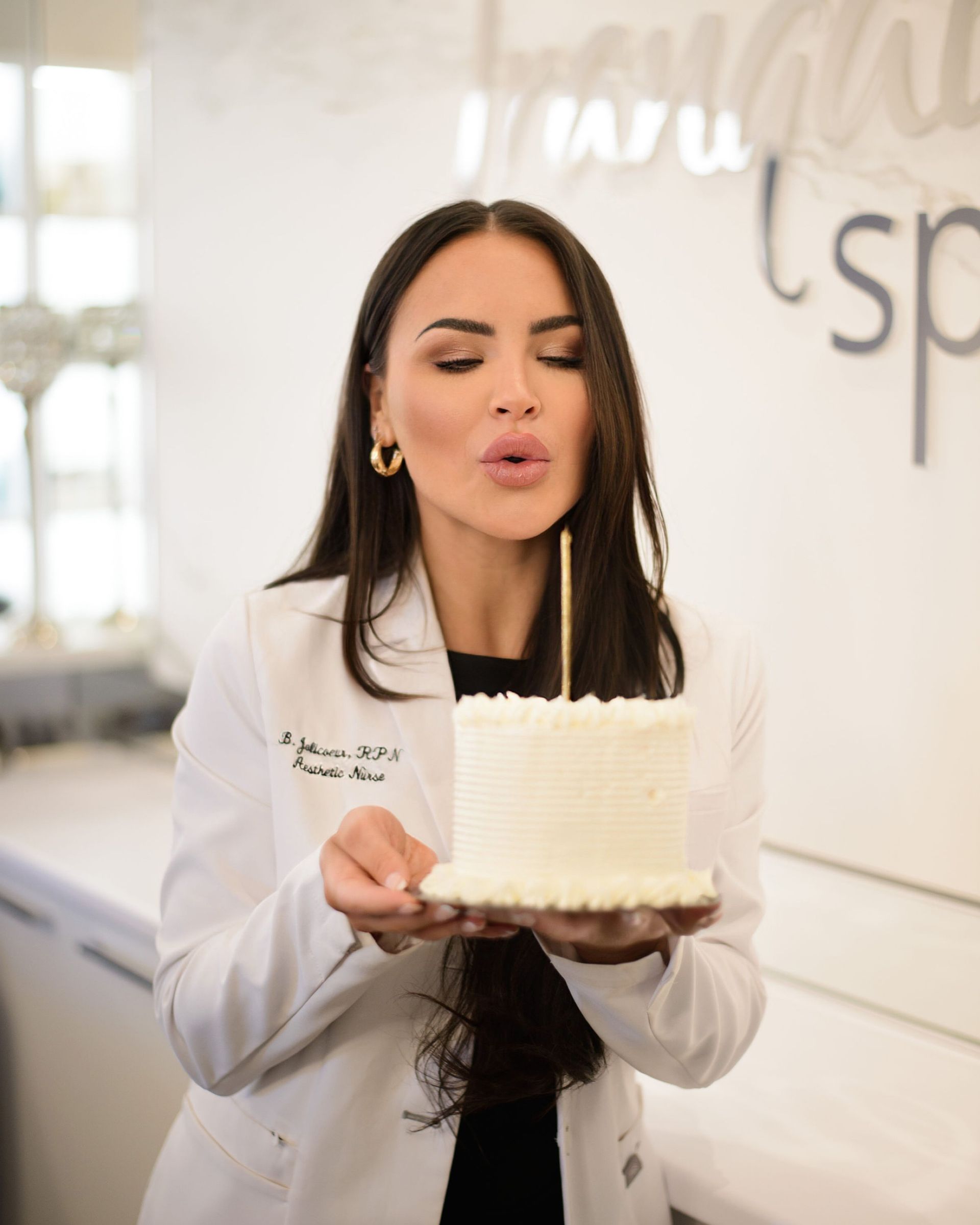 A woman in a lab coat blows out a candle on a cake