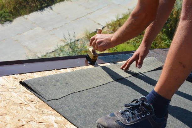 Person installing roofing shingles, using a tool to secure them. Outdoor setting with wooden surface.