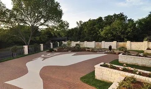 A peaceful outdoor garden with a dove-shaped inlay on a brick patio, stone planters, and a perimeter wall.