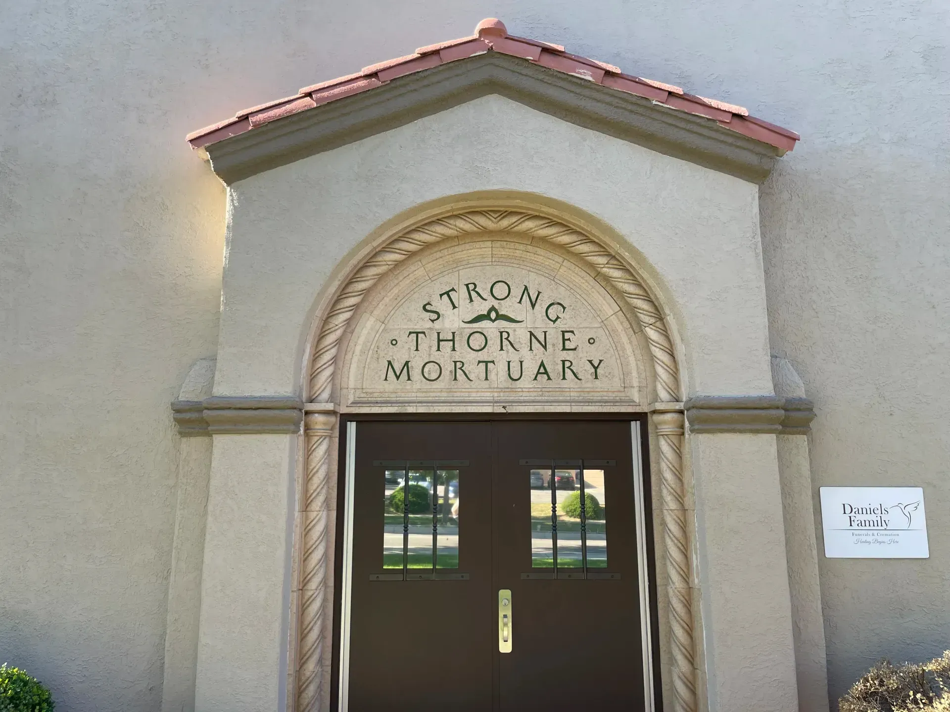 Beige stucco building with bell tower, arched windows, red tile roof, and blue sky.