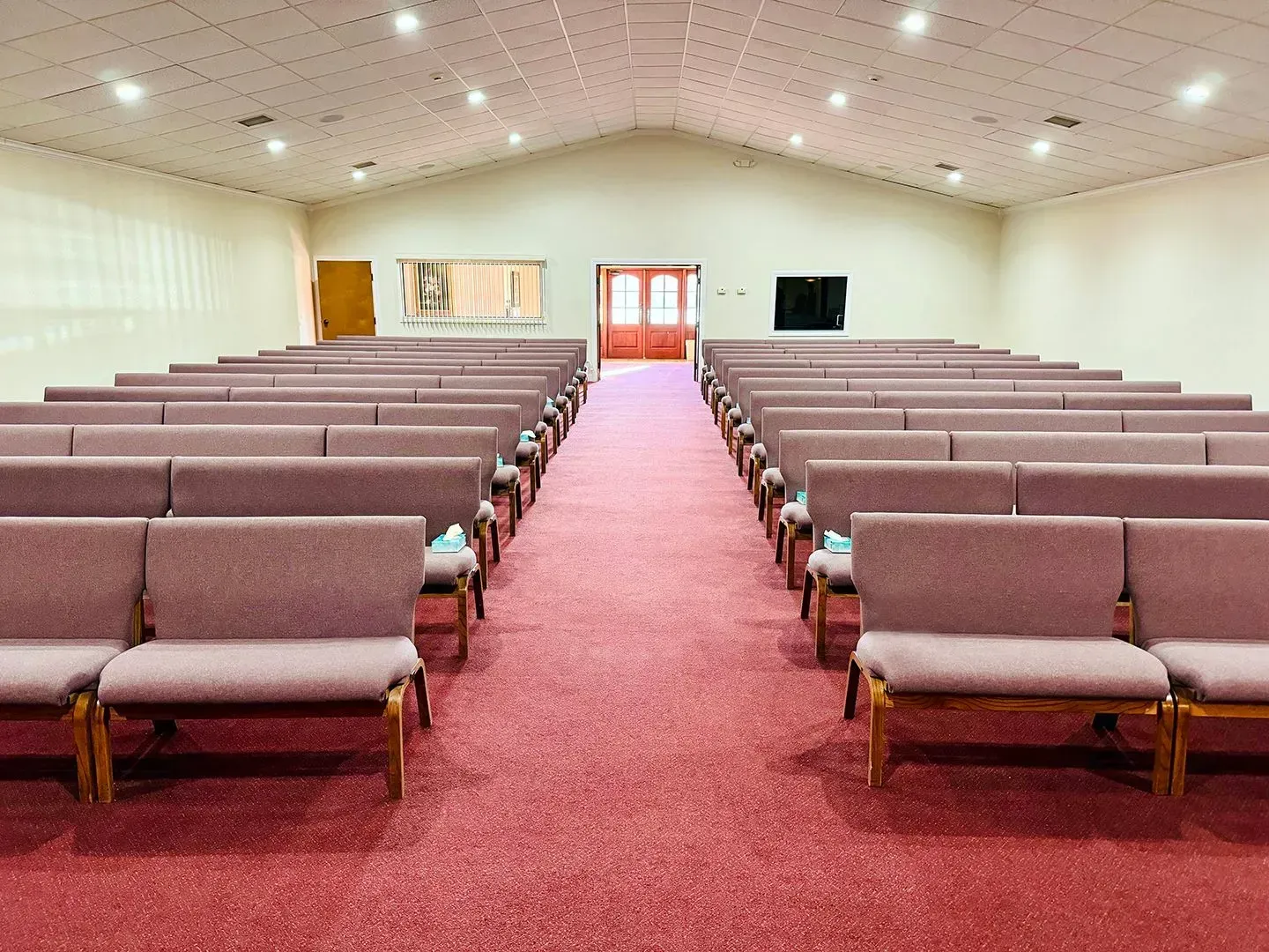 Empty church sanctuary with rows of purple pews facing an aisle, carpeted floor, and white walls.