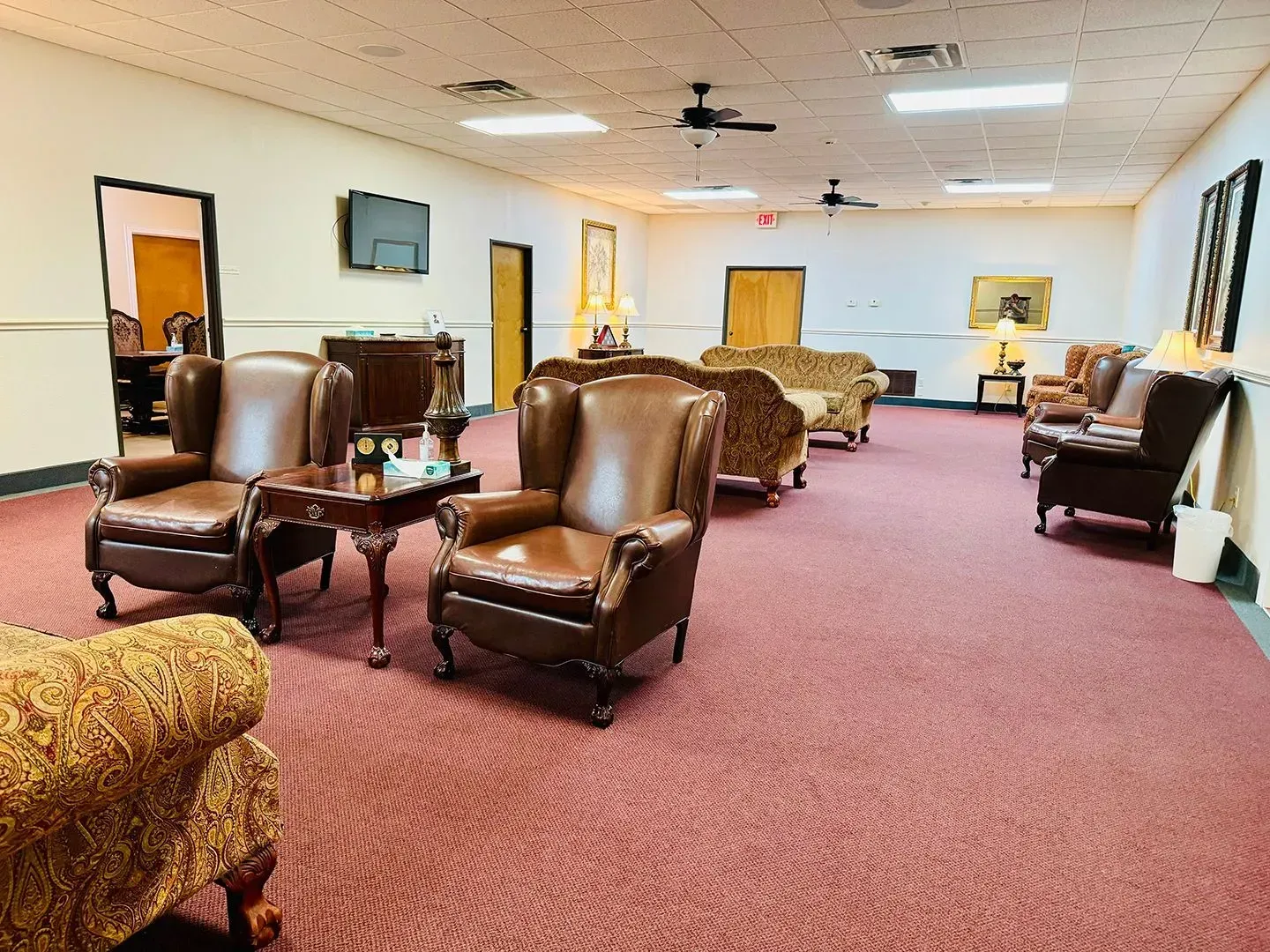 A spacious, well-lit waiting area with brown leather wingback chairs, patterned sofas, and tan carpeted flooring.