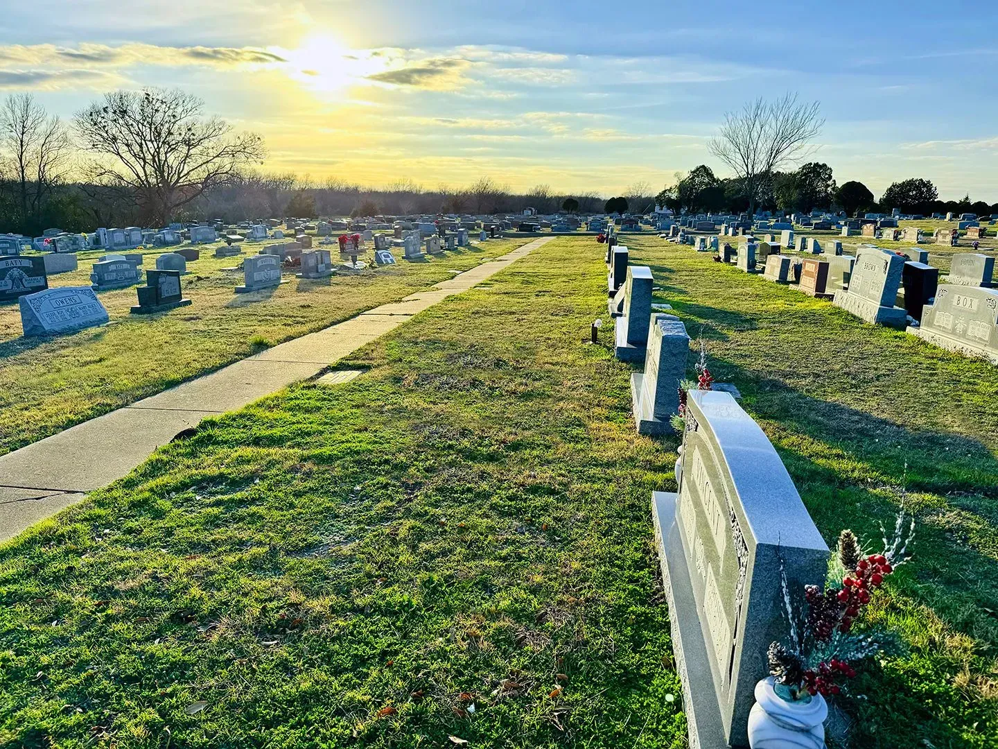Sunlight illuminates a cemetery filled with rows of headstones along a path, stretching toward the horizon.