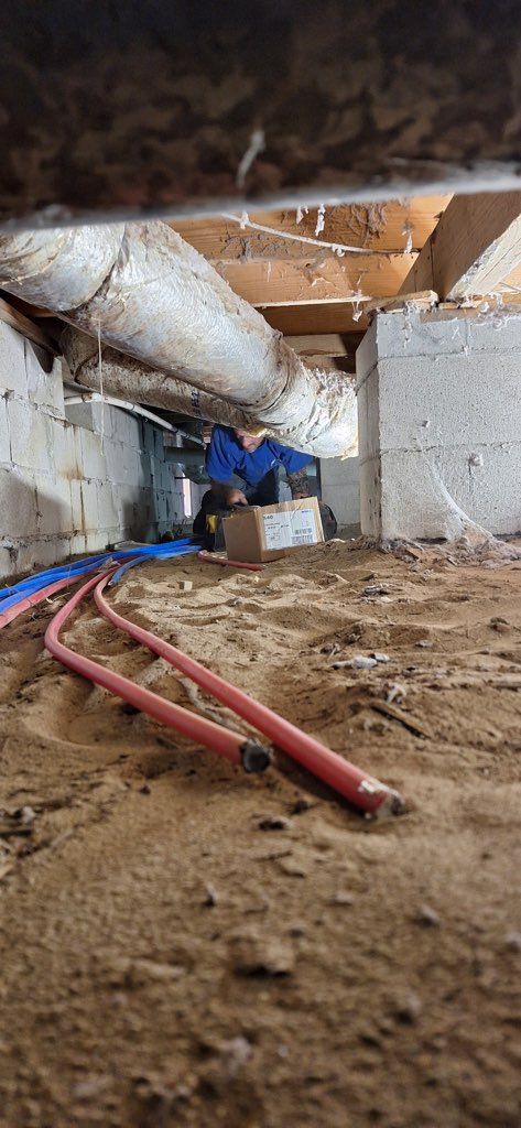 Plumber installing a kitchen faucet. He's wearing blue overalls and a tool belt, working in a white-walled kitchen.