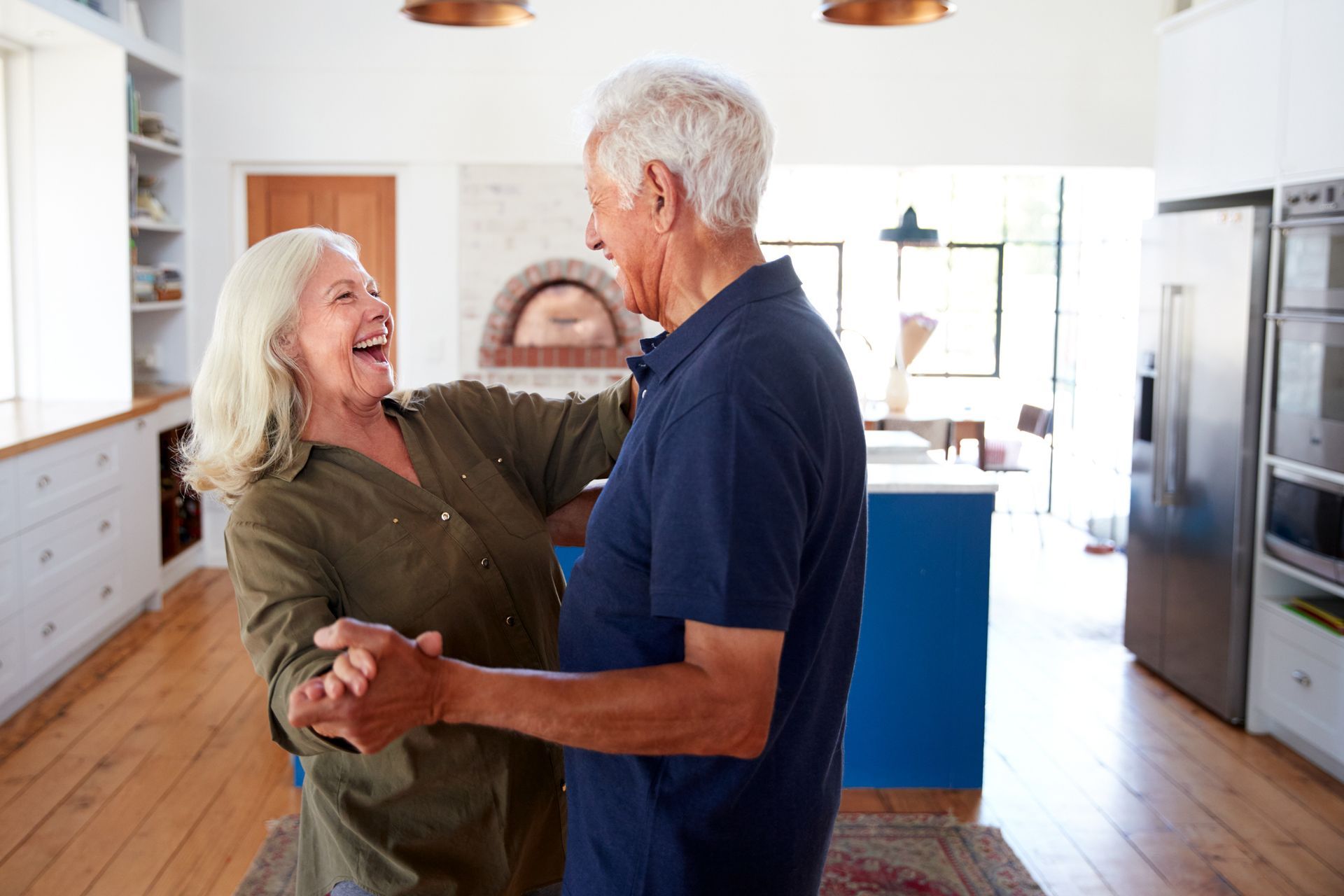An elderly couple is dancing together in a kitchen.