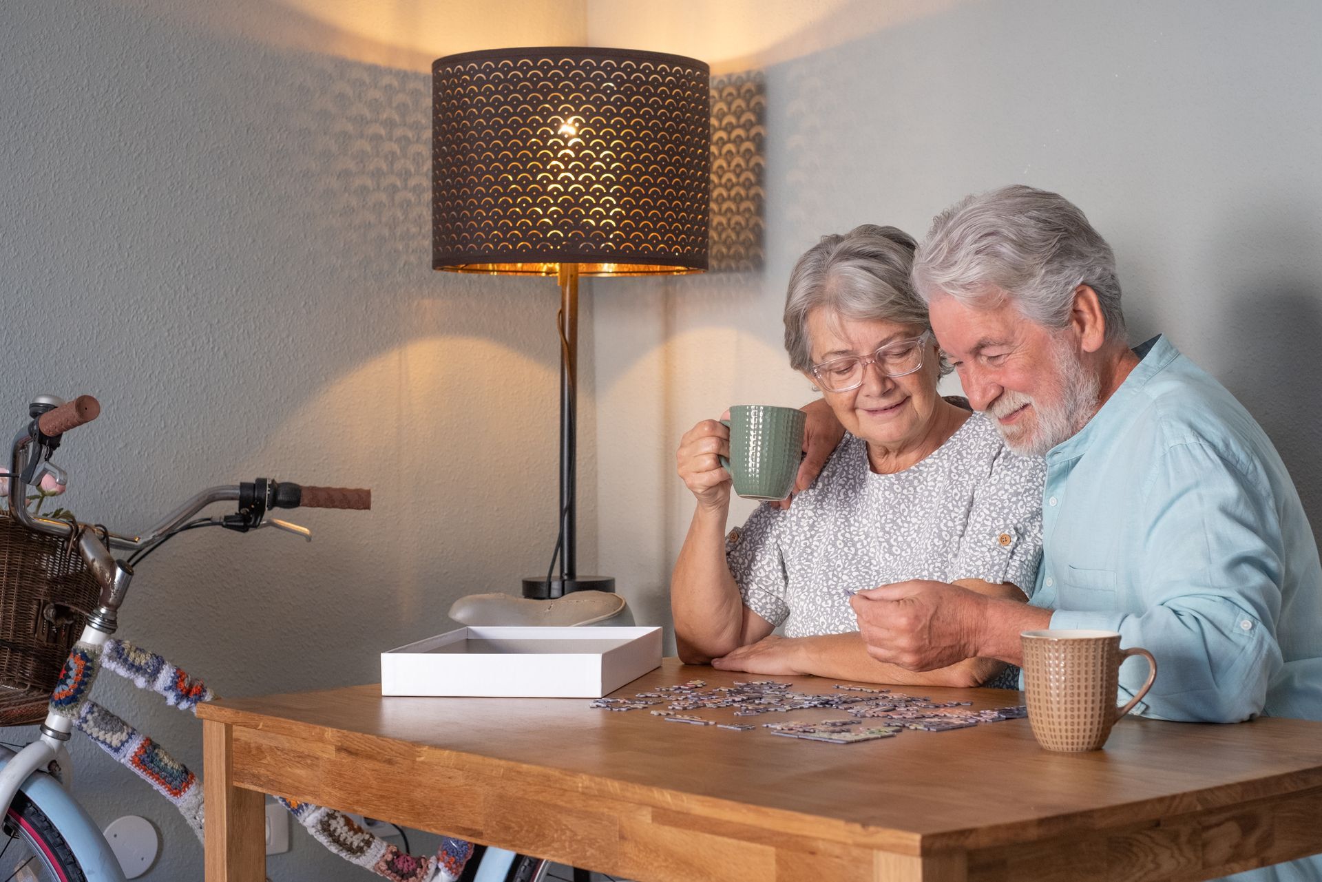 An elderly couple is sitting at a table playing a puzzle.