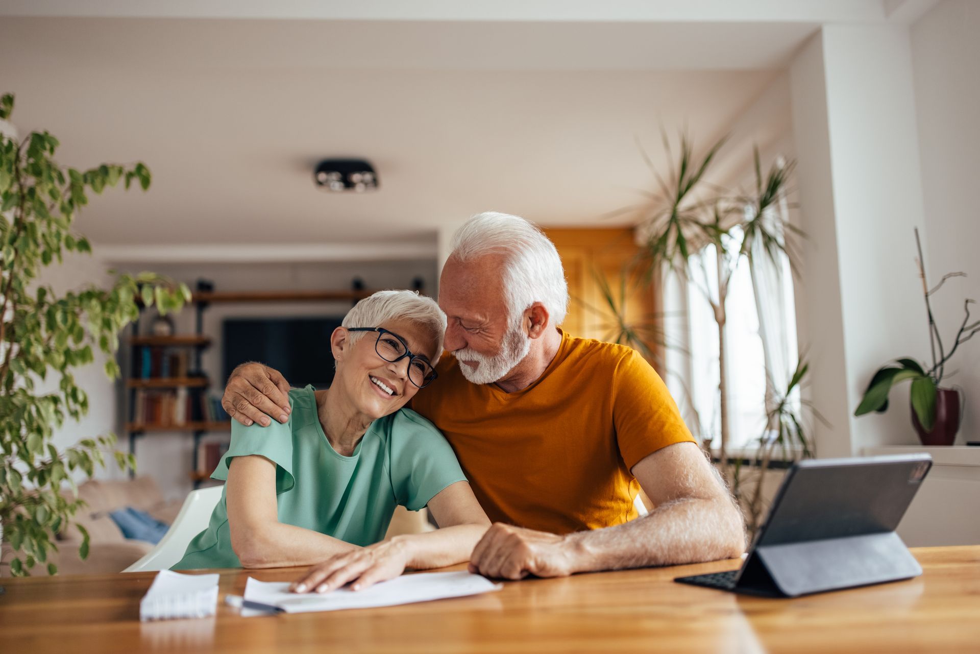 An elderly couple is sitting at a table with a tablet.
