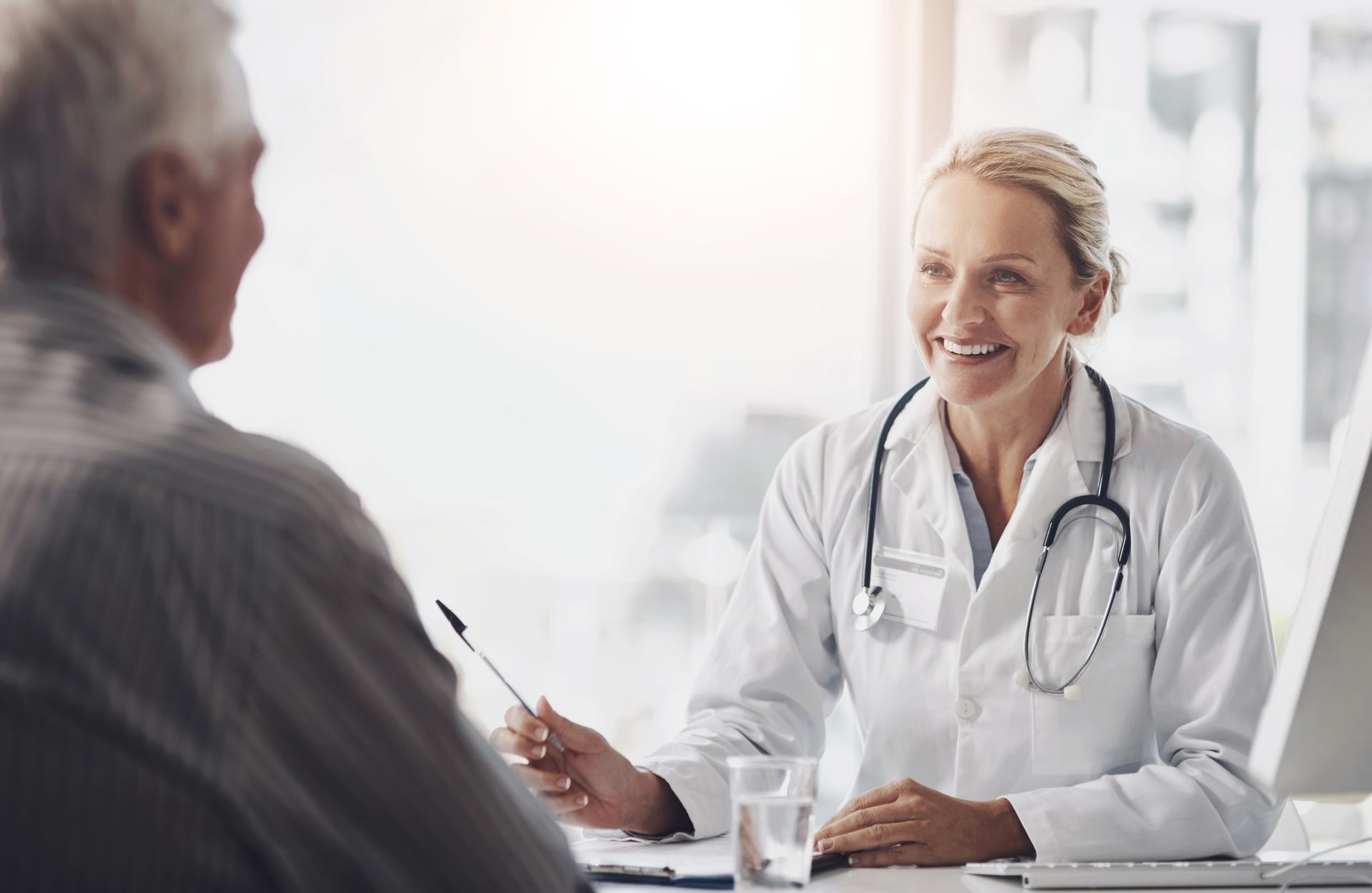 A female doctor is sitting at a desk talking to an older man.