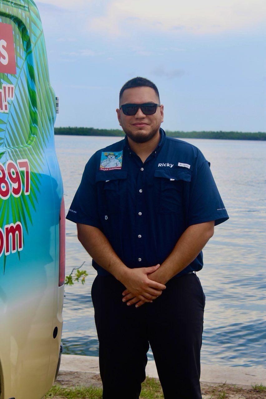 Man in sunglasses, blue shirt, and black pants stands near a van with a beach scene design by water.