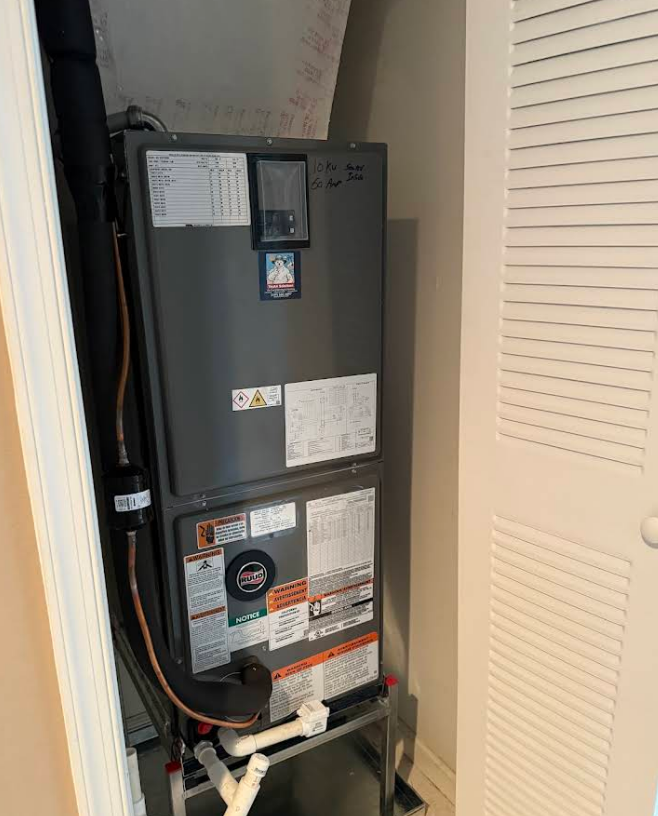A gray HVAC unit inside a white closet with a louvered door.