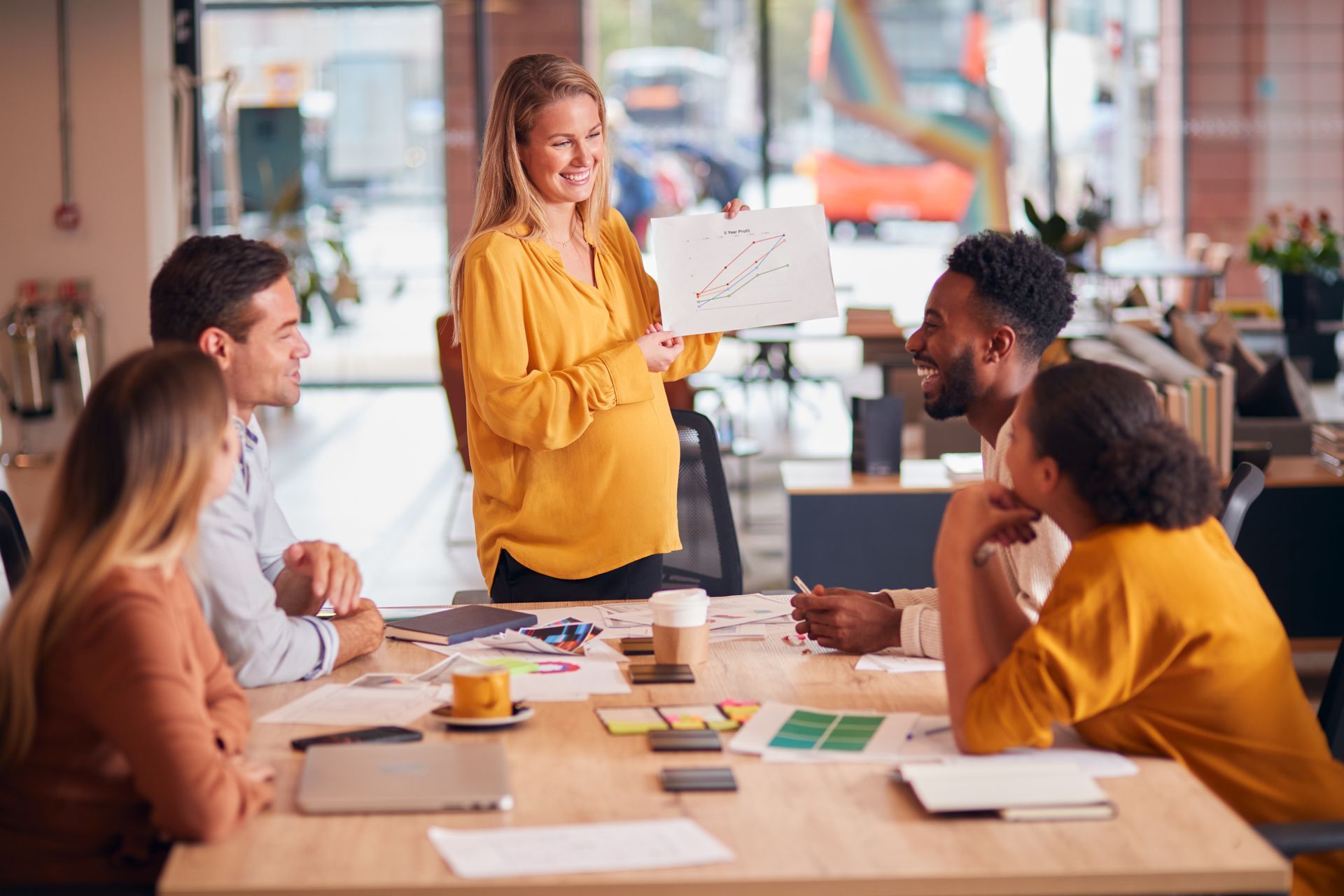 Man in orange shirt gestures, talking to another man with arm around him on a couch.