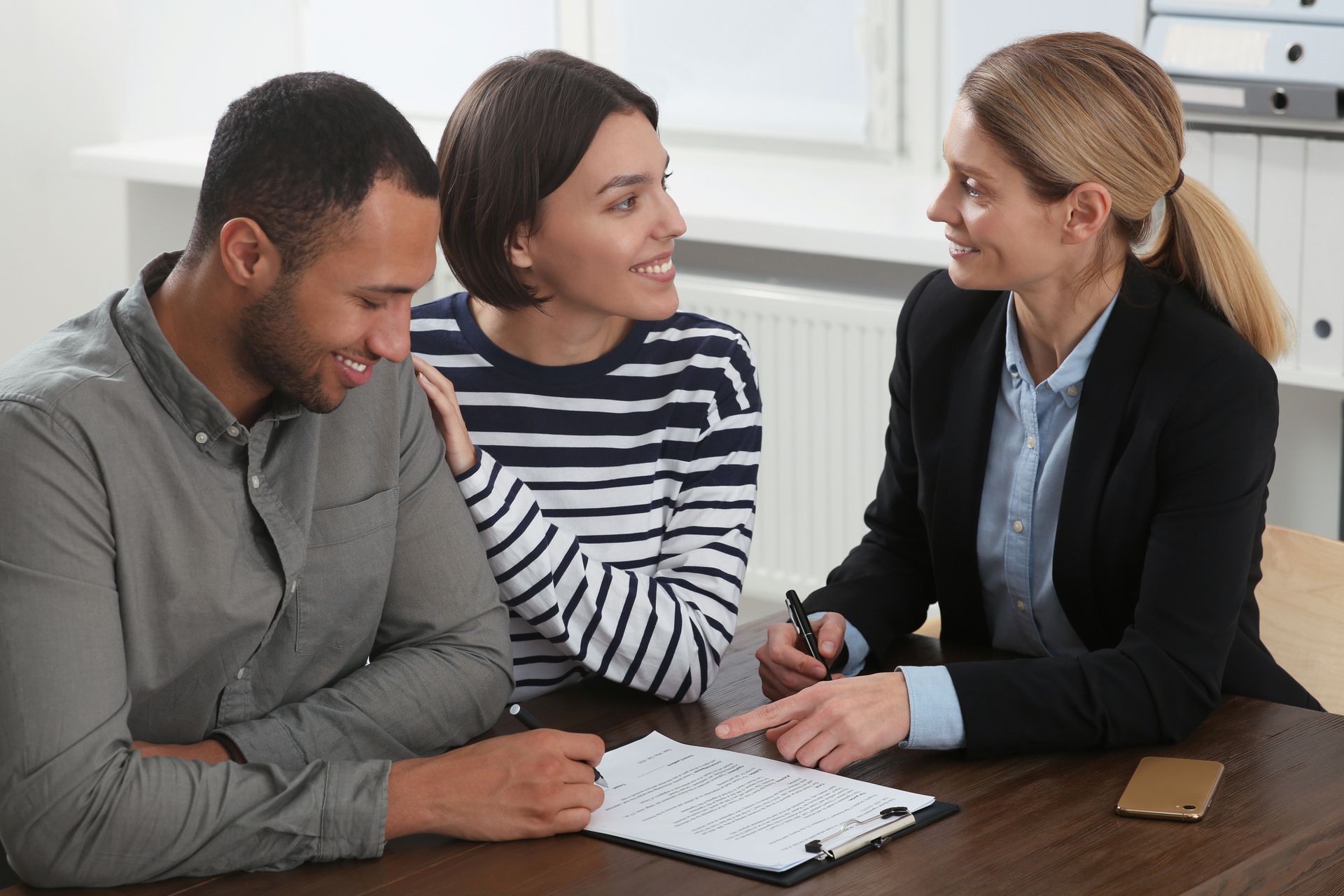 Couple signing document with advisor at desk.