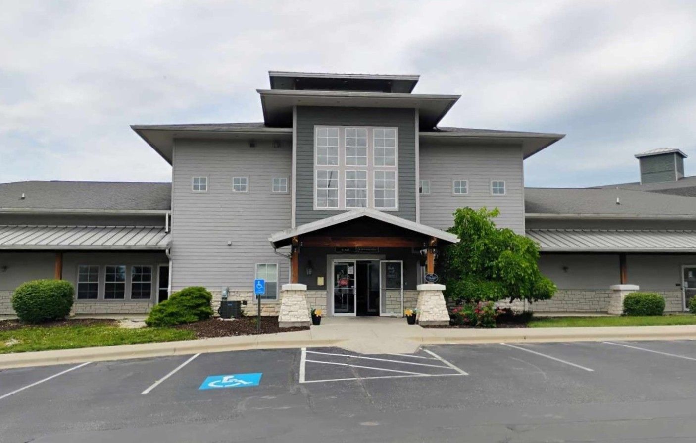 Gray building with central entrance, accessible parking, and landscaped greenery.