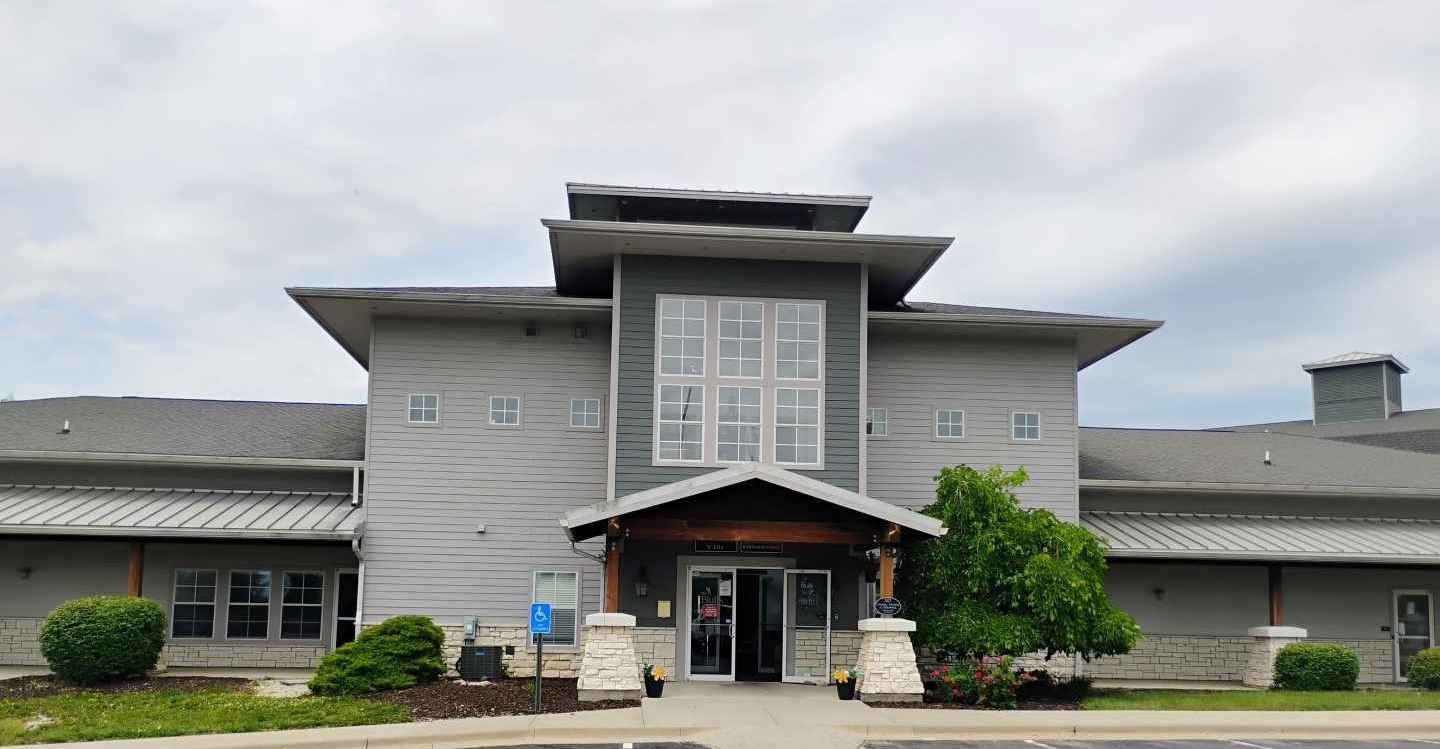 Gray building with a unique tiered roof, large windows, and a welcoming entrance under a wooden overhang.