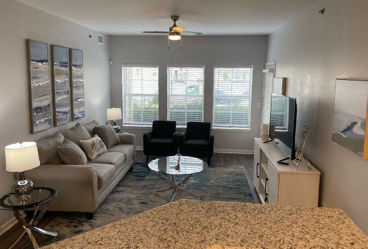 Living room with beige sofa, two black chairs, three windows, and art.