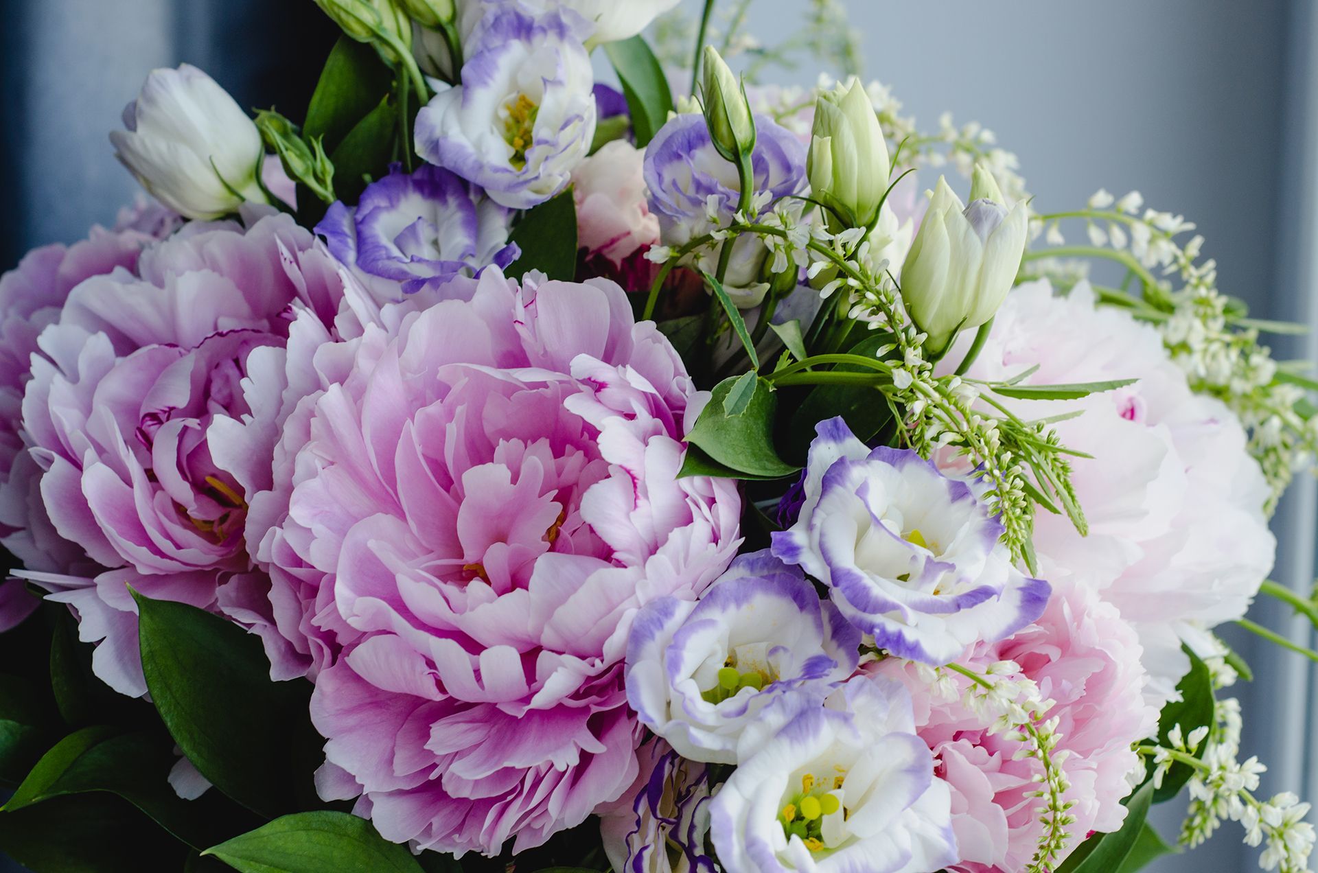 A bouquet of fluffy light-purple peonies and white eustoma flowers with purple-edged petals and green foliage.
