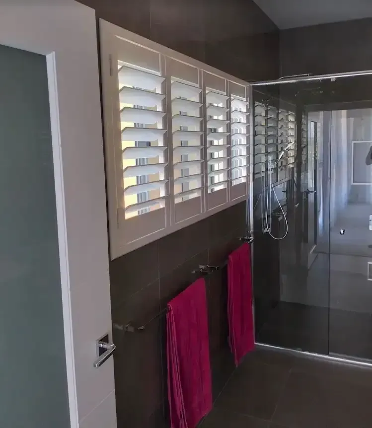 Bathroom With White Shutters, Pink Towels, and a Glass Shower Door — Seaview Blinds & Shutters in Woodbury, QLD