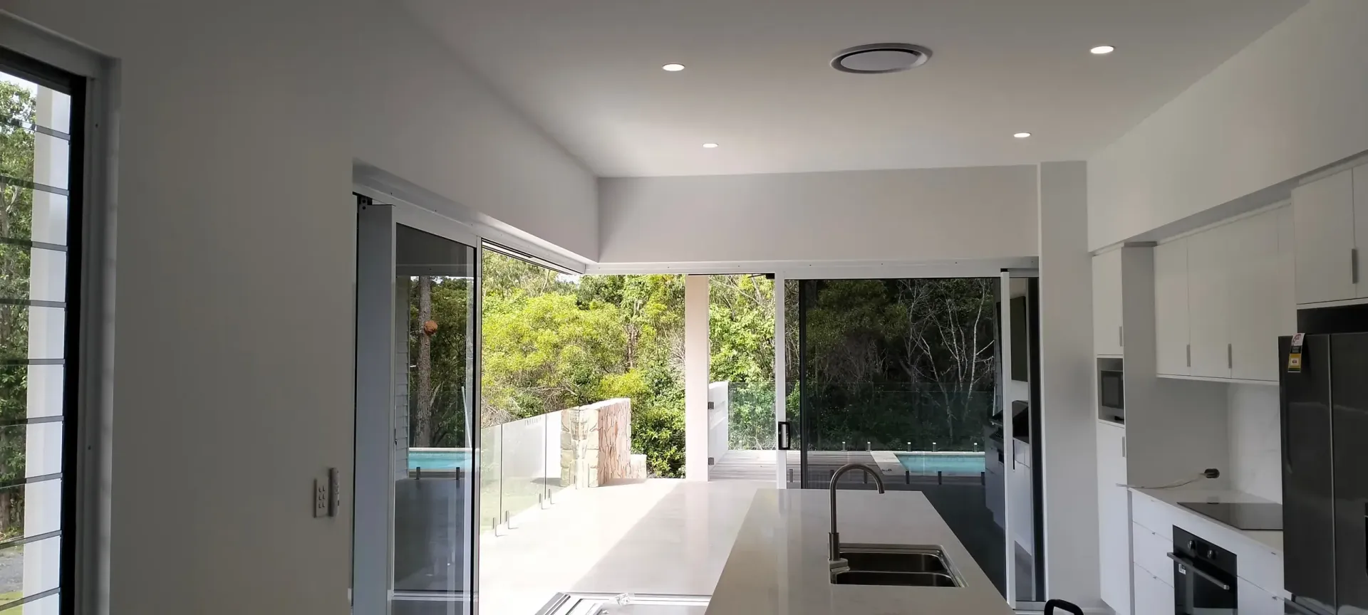 Interior View of a Modern Kitchen With White Cabinetry and Sliding Glass Doors That Open to a Green Outdoor Space — Seaview Blinds & Shutters in Woodbury, QLD