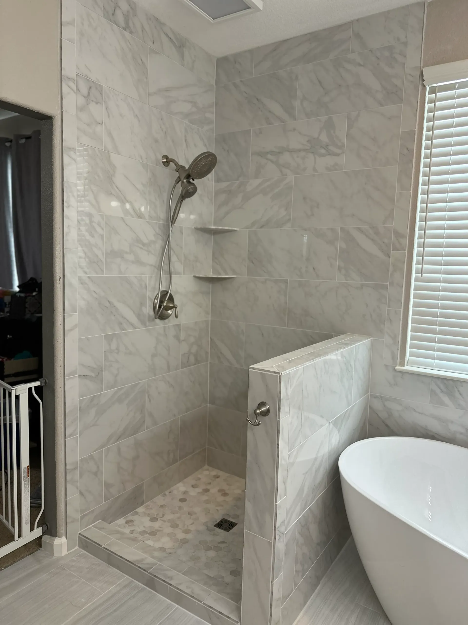Tiled shower with built-in shelves, handheld showerhead, and a small pebble floor.