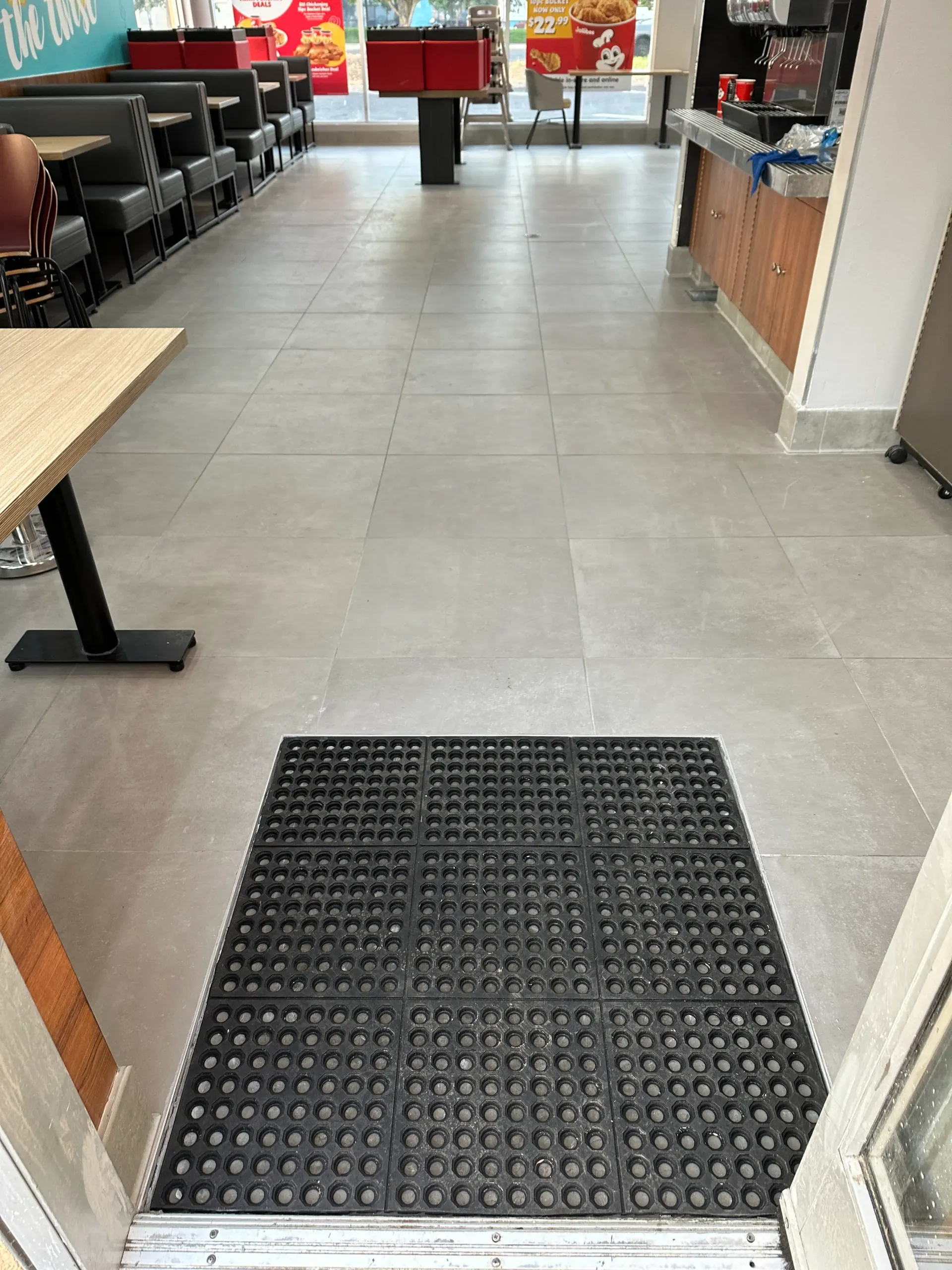 A black rubber mat inside a fast-food restaurant doorway, leading to seating and counter areas.