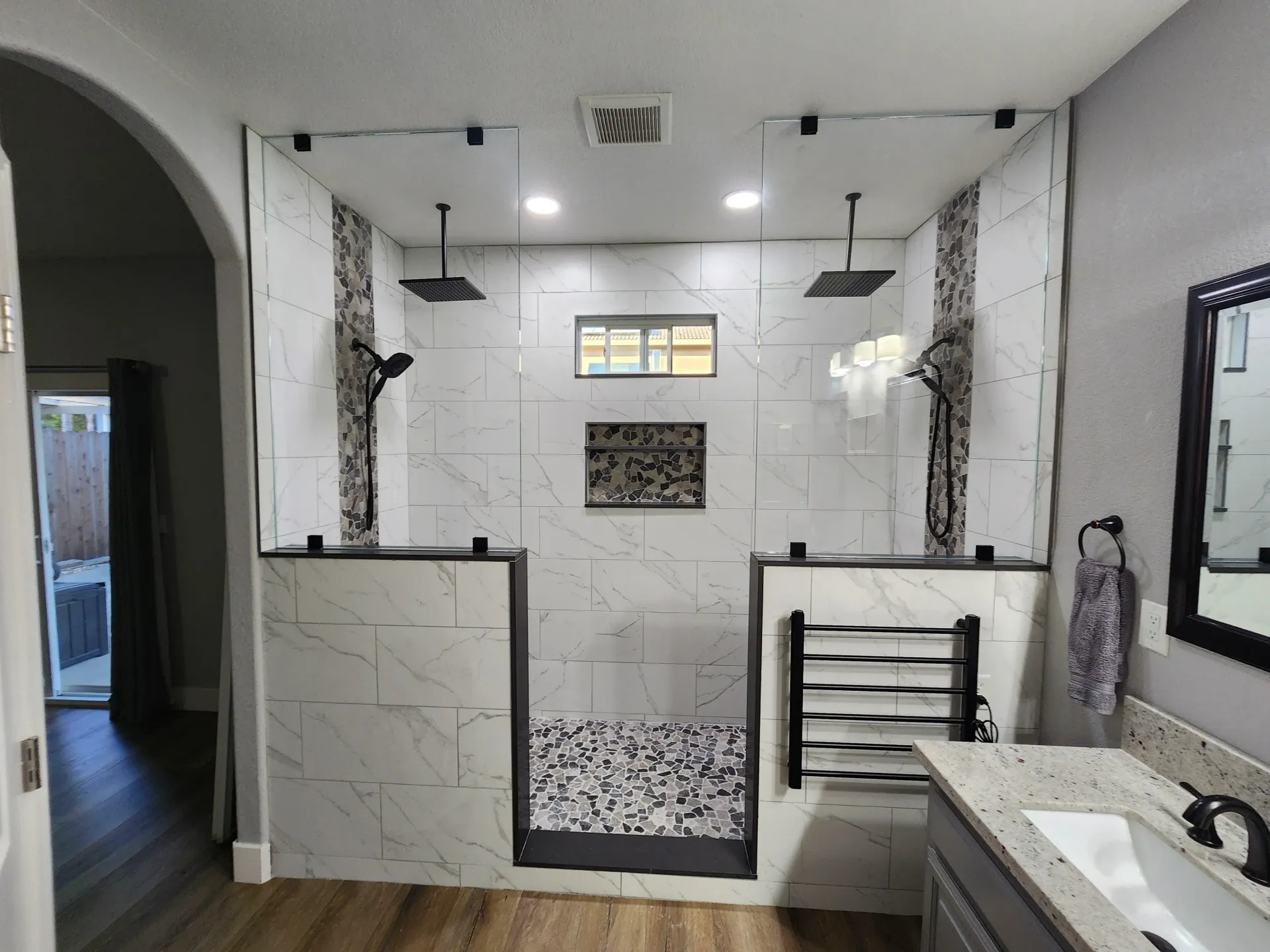 Modern bathroom with dual showers, white marble tile, glass enclosures, and a grey vanity.