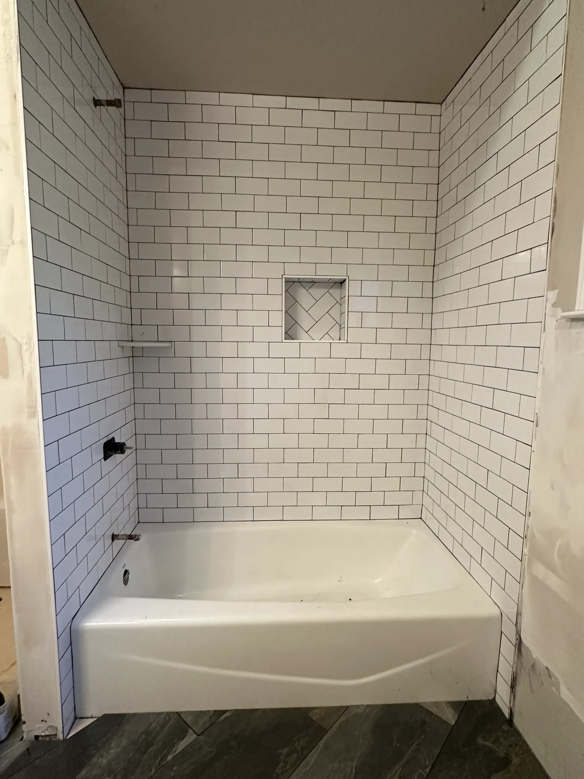 White tiled shower with a built-in bathtub and a recessed shelf, under construction.