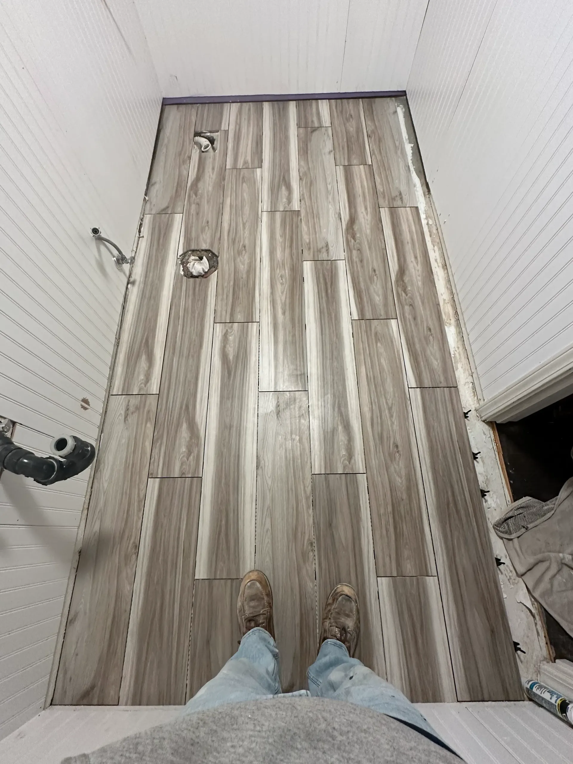 Person standing in a bathroom with new wood-look floor tiles installed.
