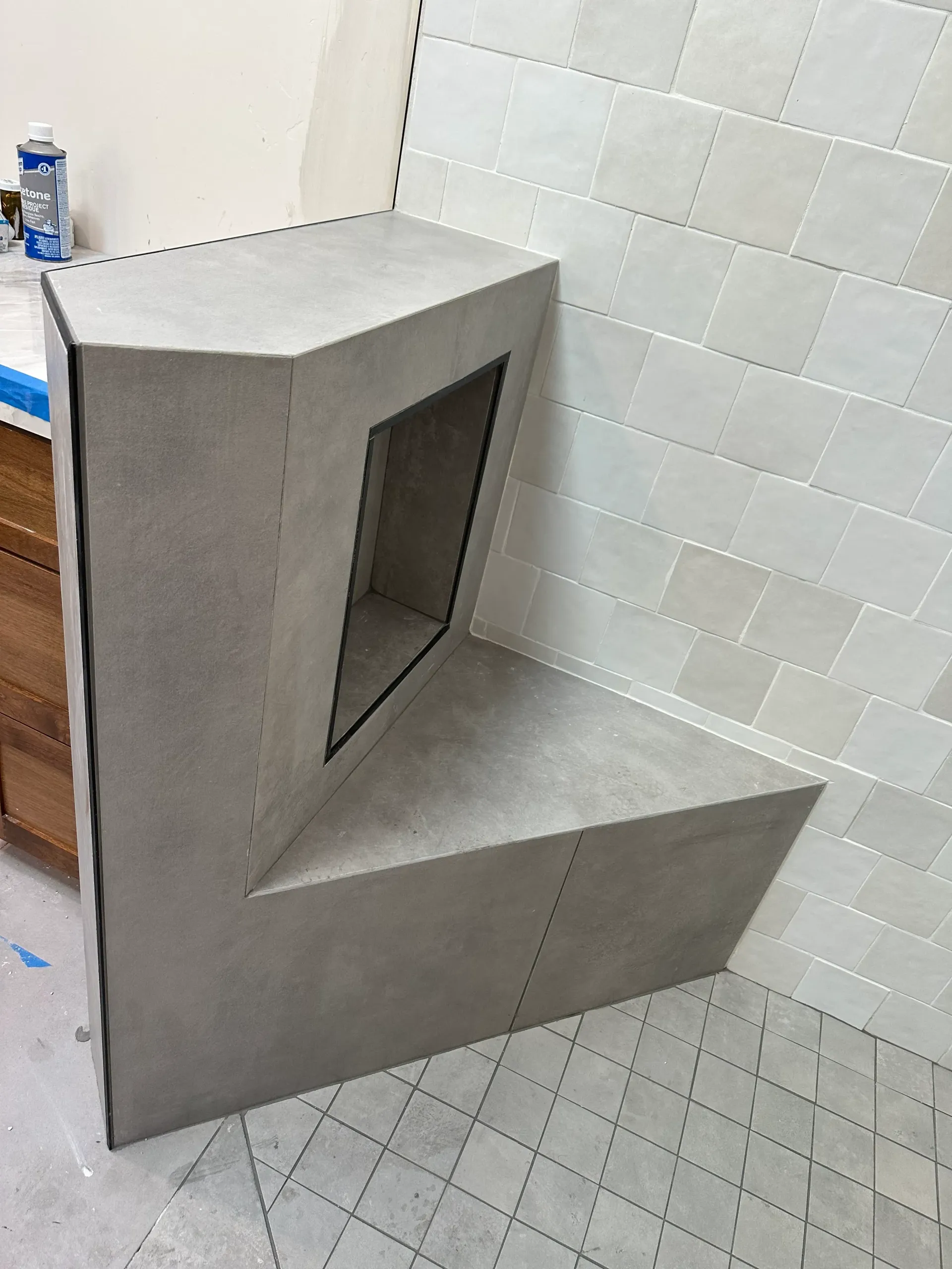 Gray stone corner bench with an open niche, against a tiled wall.
