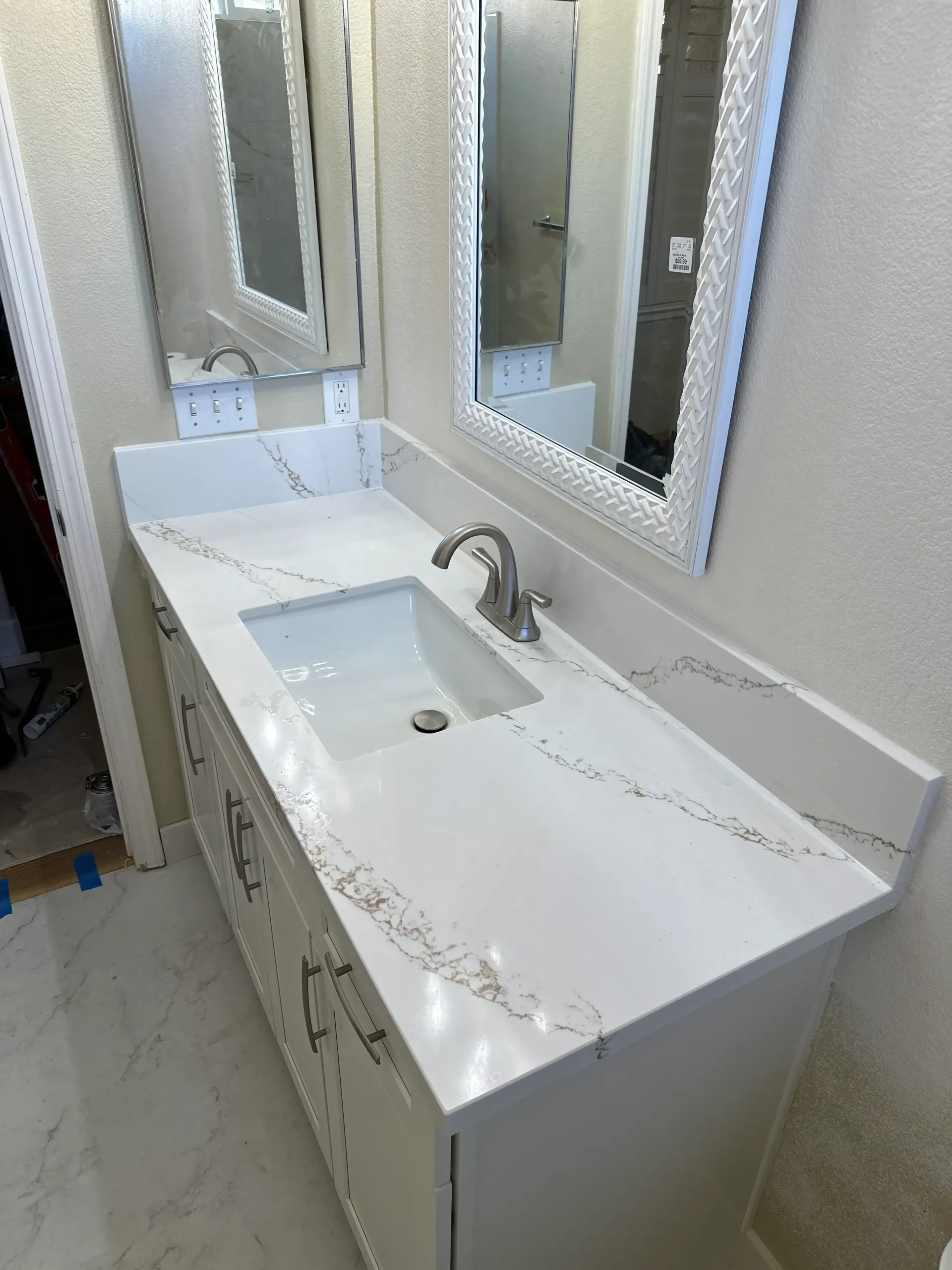 White bathroom vanity with a quartz countertop, sink, and framed mirror.