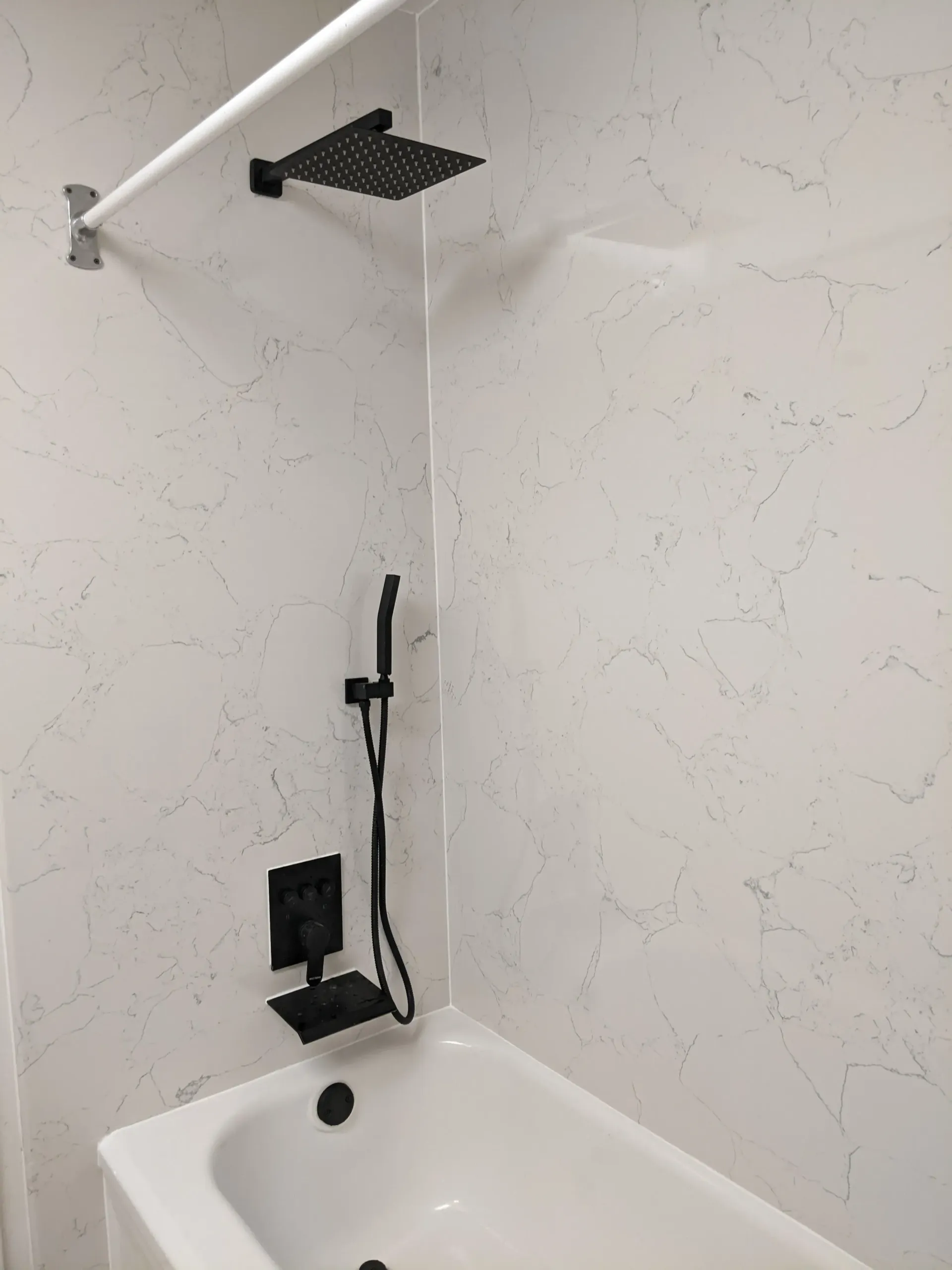 Black shower fixtures on a white marbled wall above a white bathtub.