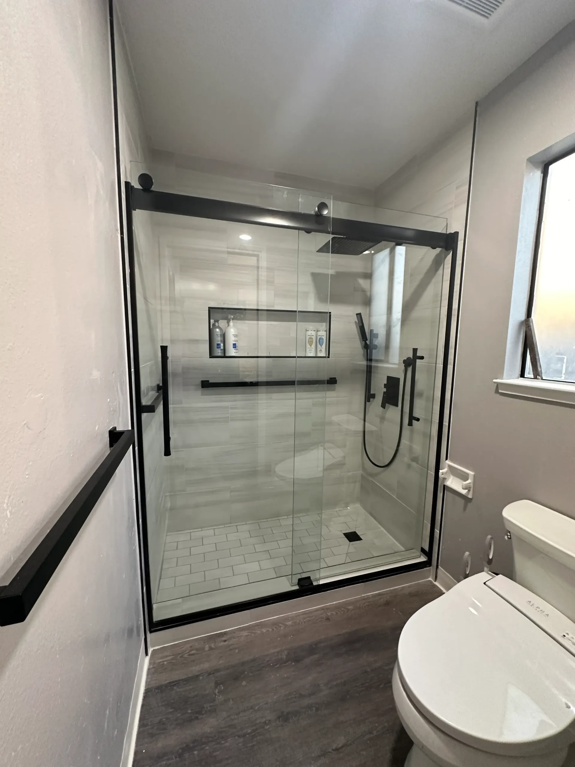 Modern bathroom with black-framed glass shower, toilet, and dark gray flooring.