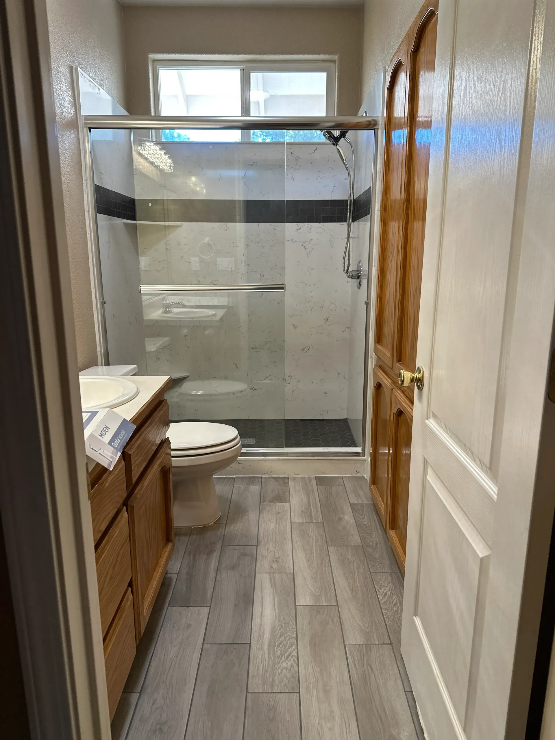 Bathroom with a shower, toilet, vanity, wood door, and gray tiled floor.