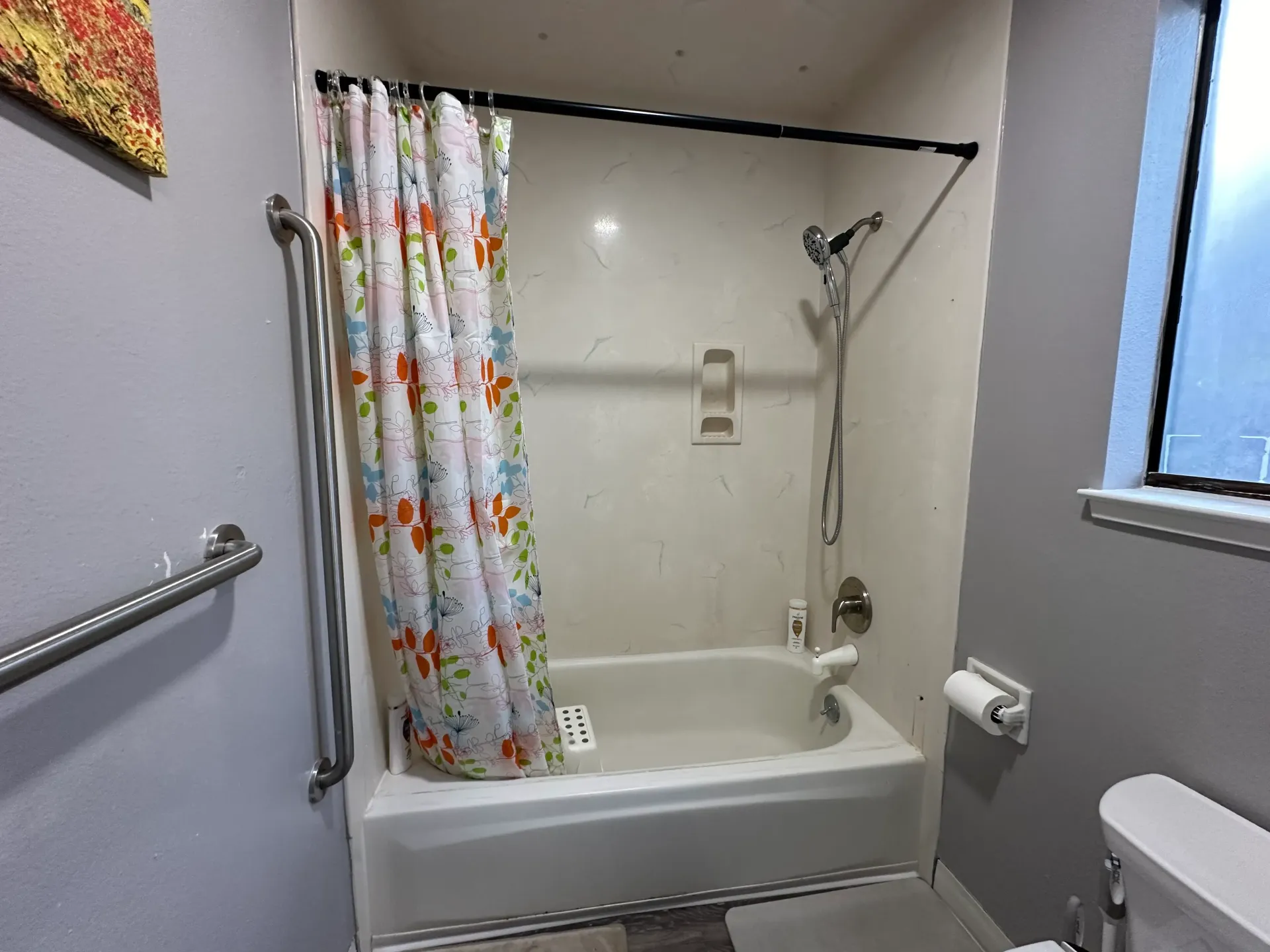 Bathroom with shower, floral shower curtain, grab bar, and toilet.