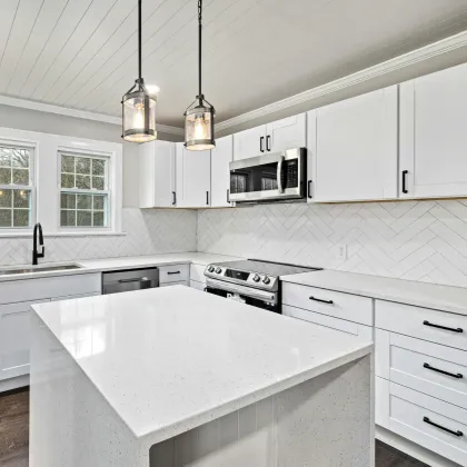 White kitchen with island, cabinets, and stainless steel appliances. Two pendant lights hang over the island.
