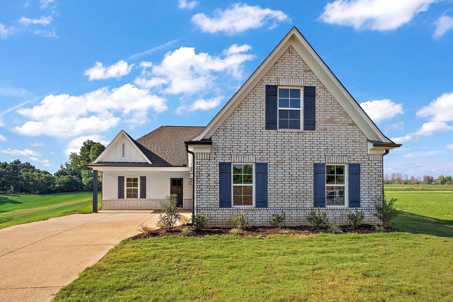 A white brick house with blue shutters is sitting on top of a lush green field.
